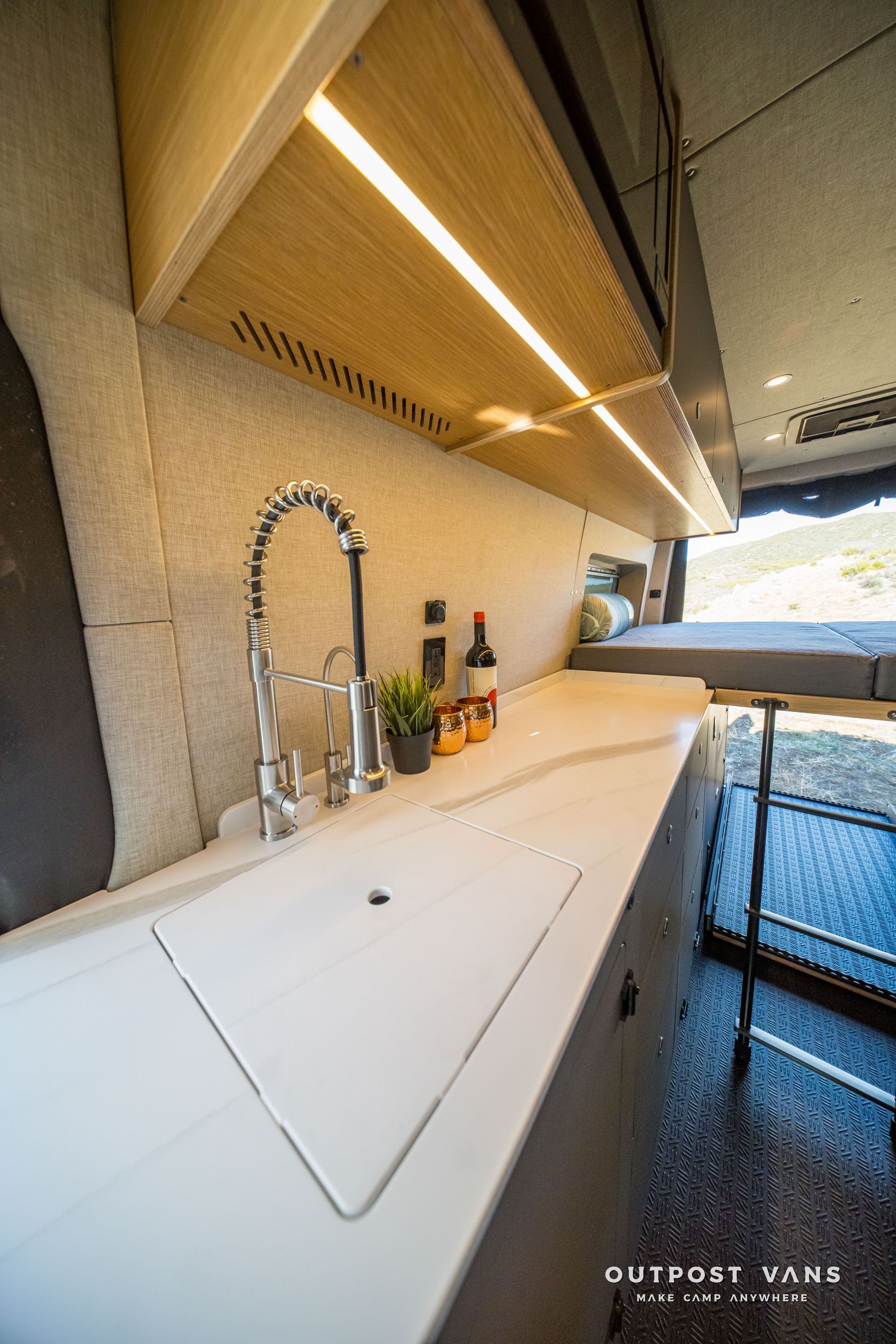 Van kitchen interior with sink, faucet, countertop, overhead lighting, and cabinets.