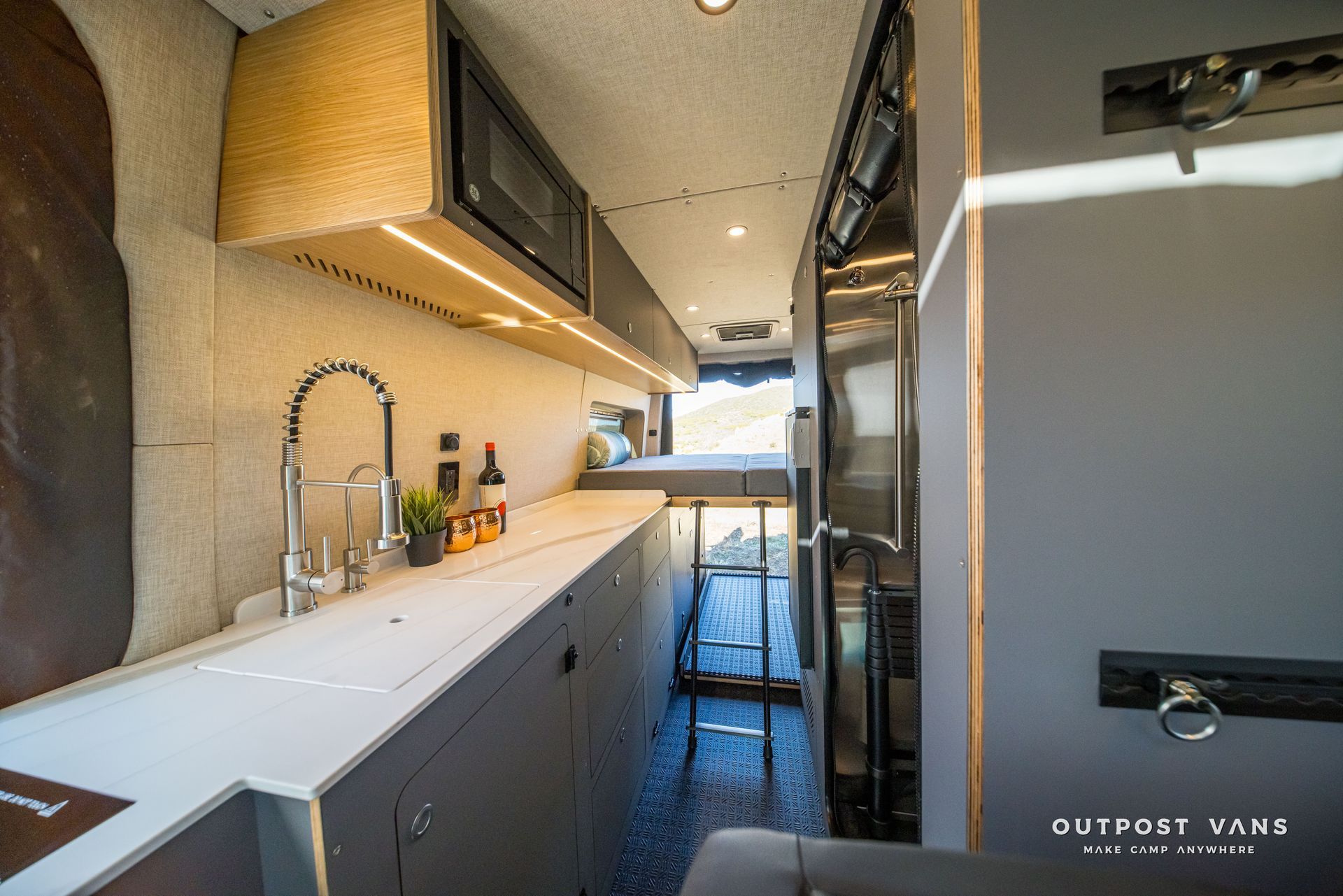 Interior of a camper van with a kitchen area, featuring a sink, countertop, cabinets, and a microwave.