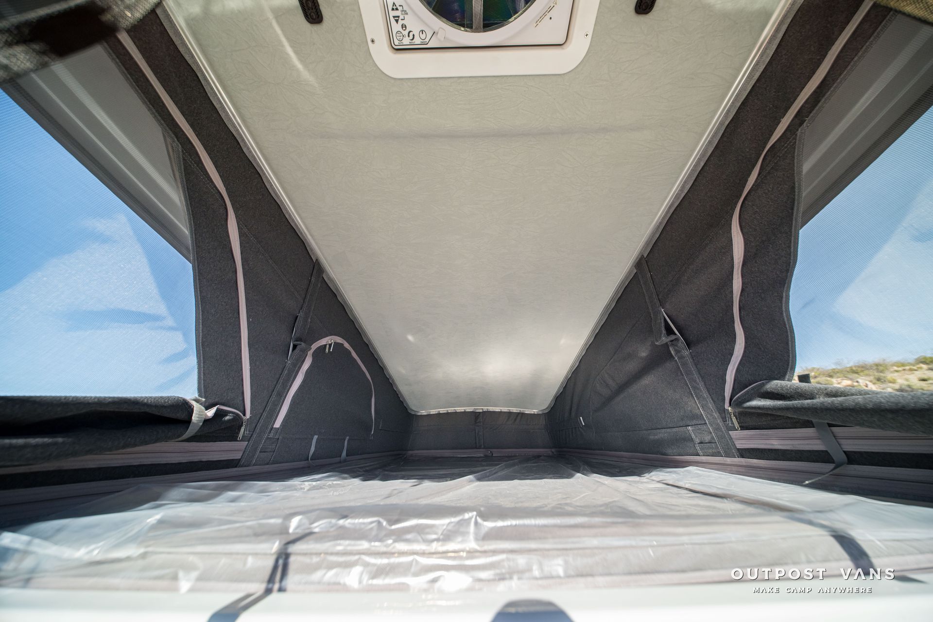 Inside view of a campervan pop-up roof. Beige ceiling and gray walls with mesh windows, open to the sky.