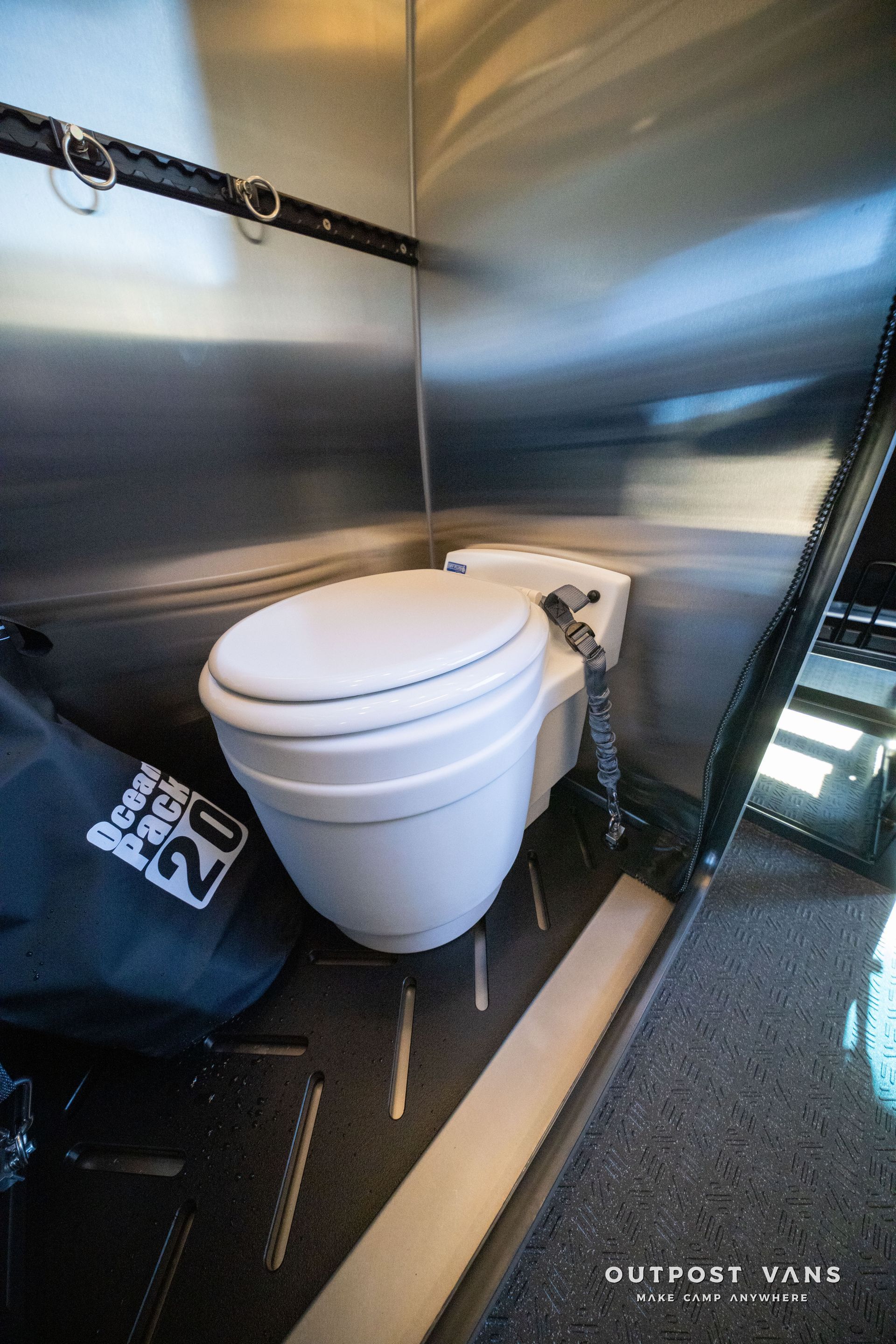 White toilet inside a small, metal-lined space. Black floor and wall accents.