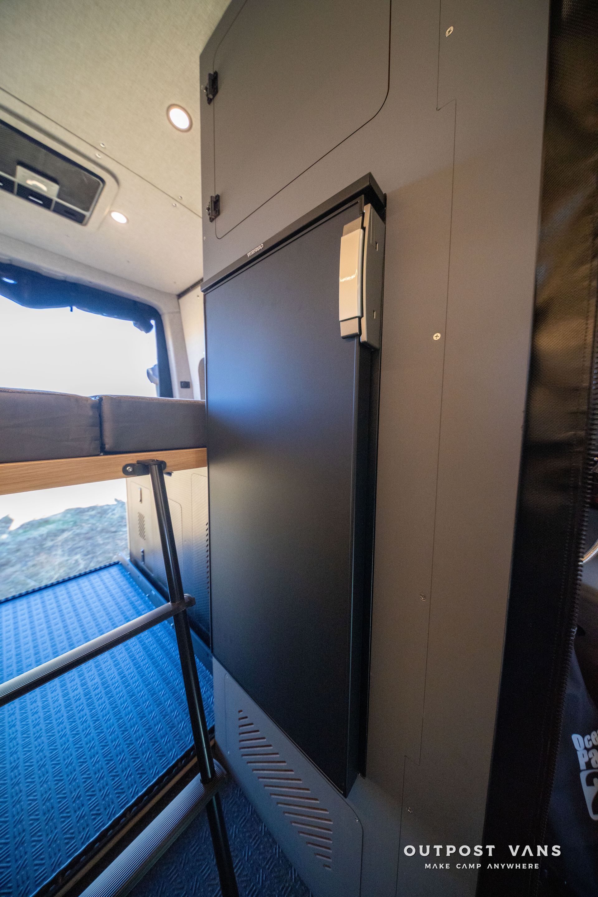 Black refrigerator door in a van. Bed and storage visible.