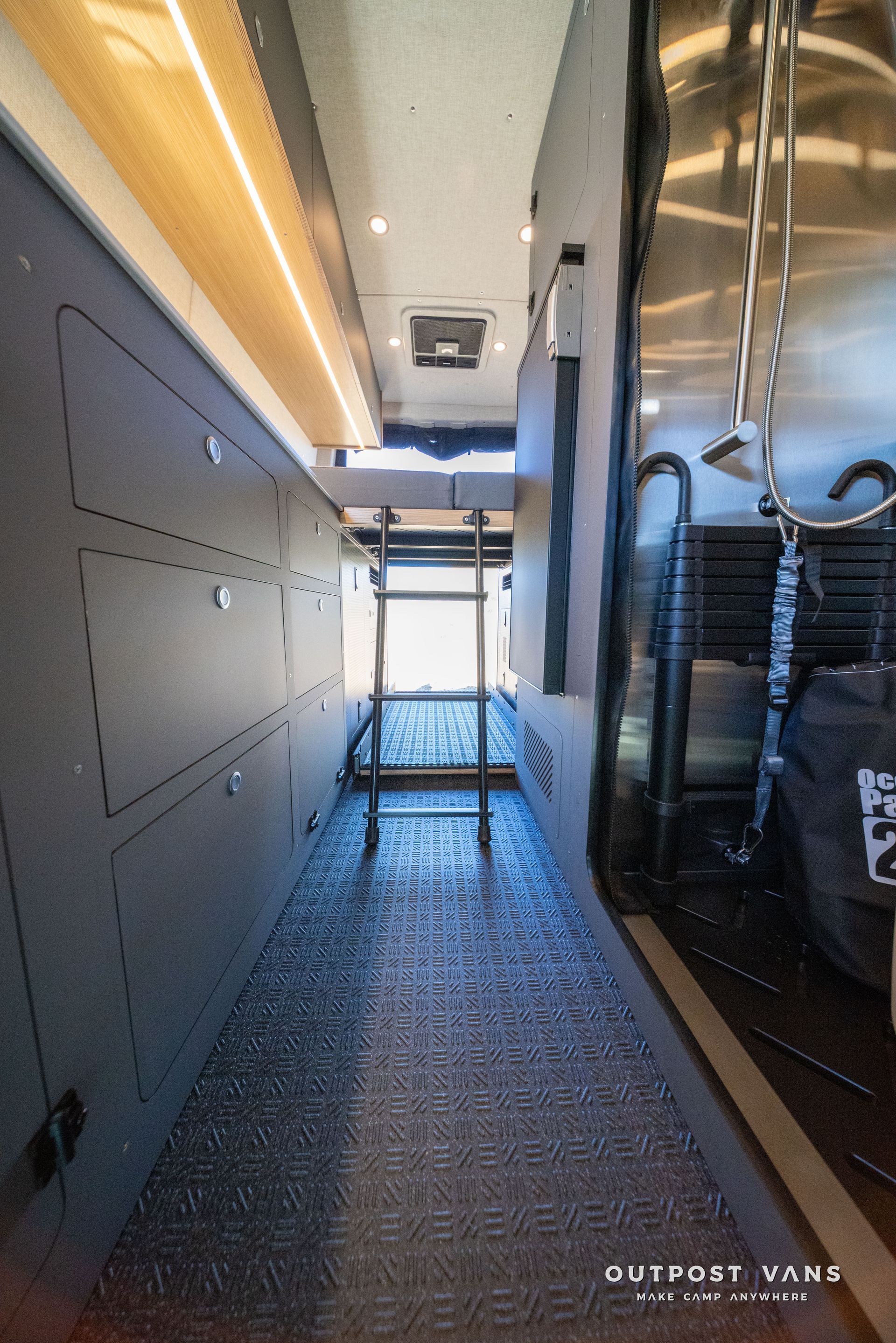 Interior of a camper van with a narrow walkway, storage on the left, and ladder leading up.