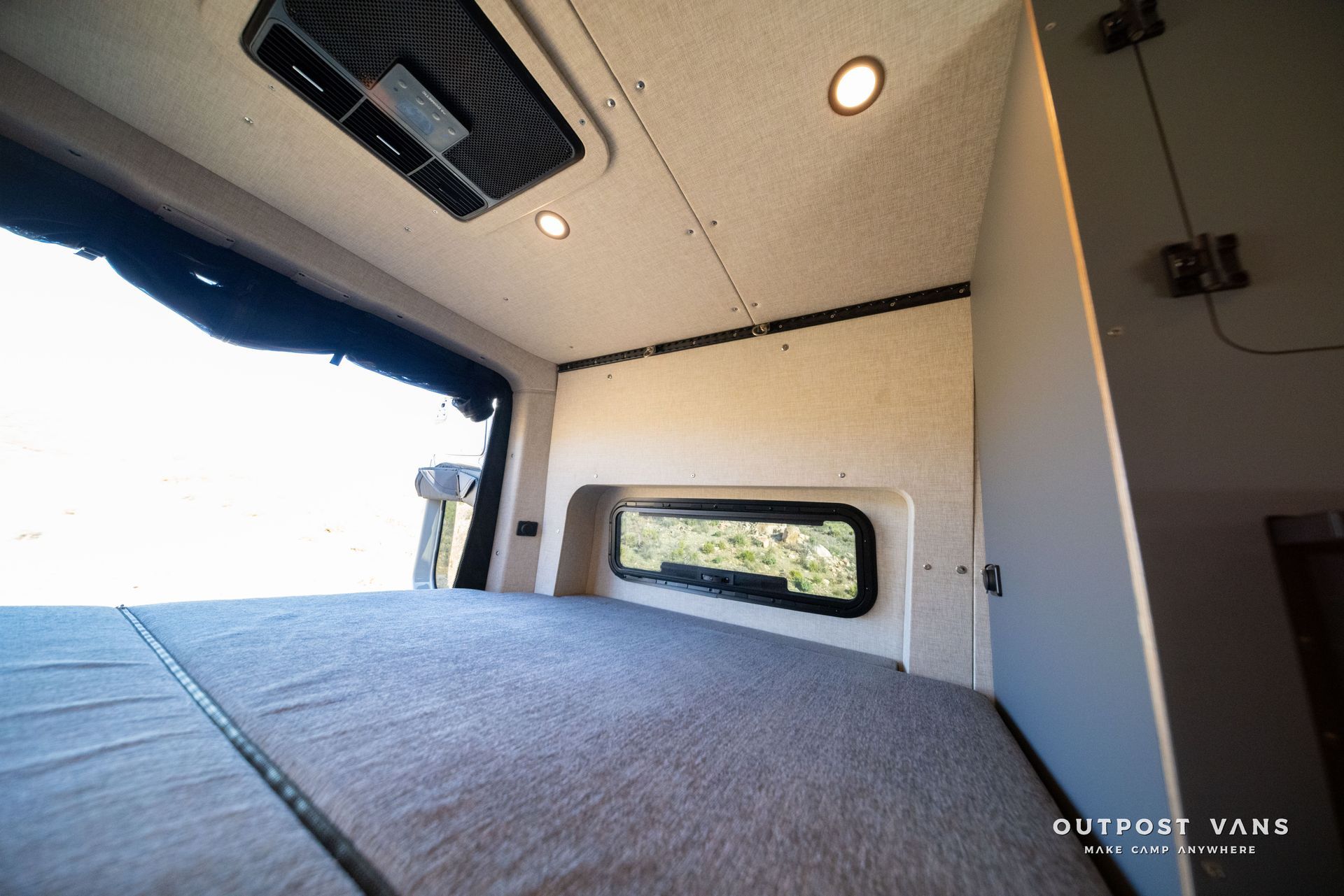Interior of a van with a bed, small window, and ceiling lights.