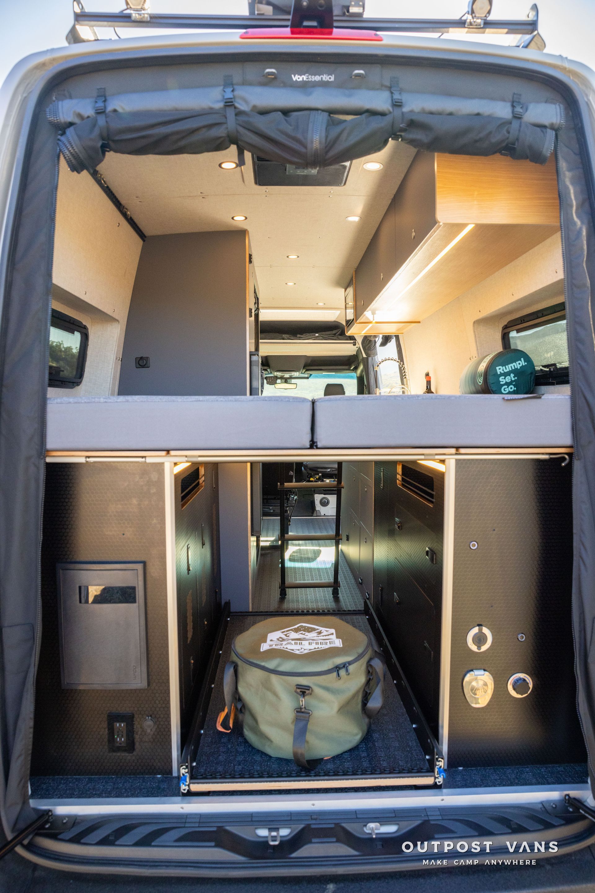 Interior view of a camper van with a bed platform, storage drawers, and a cooler bag.