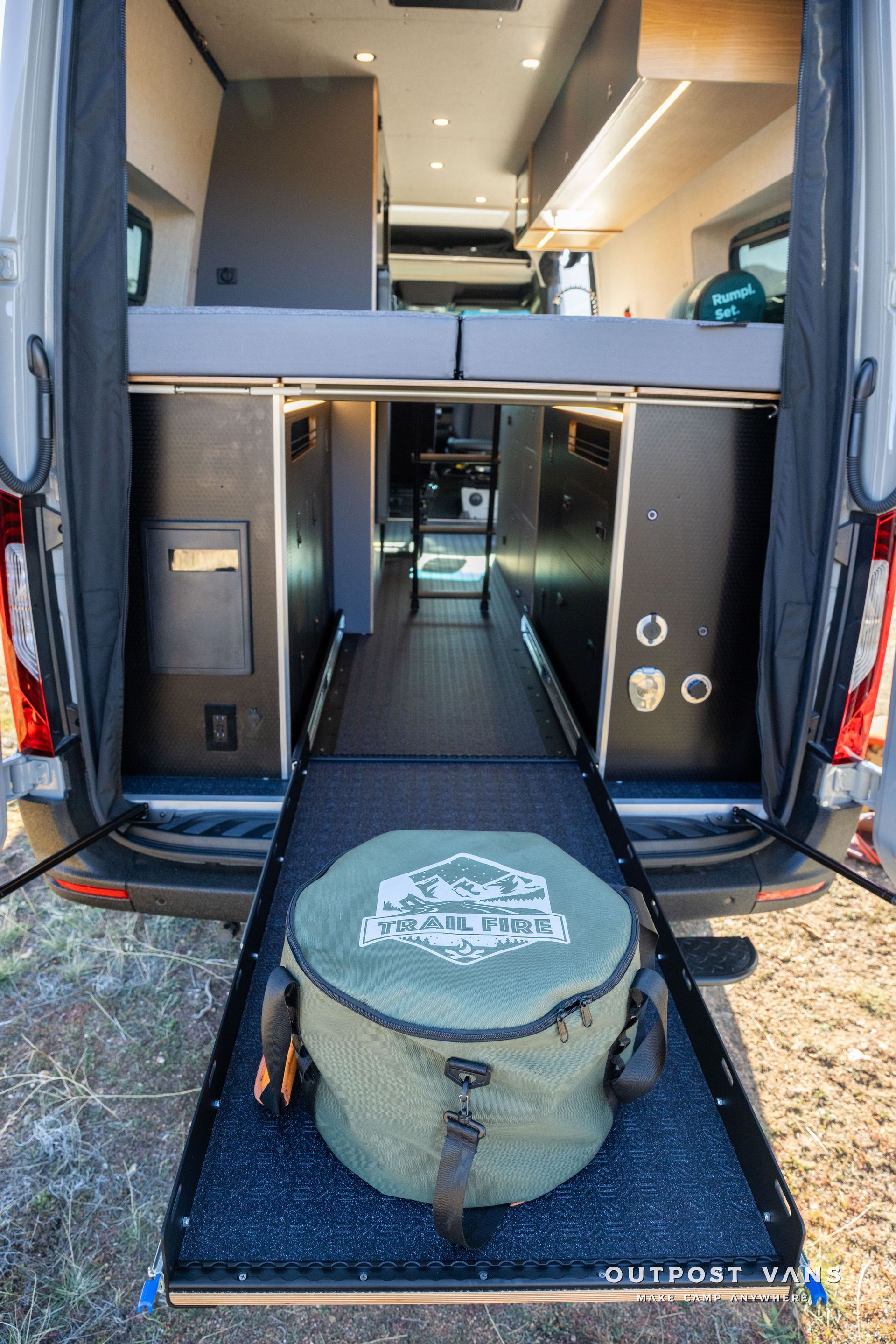 Van interior with open rear doors, revealing a pull-out tray with a green camping bag.