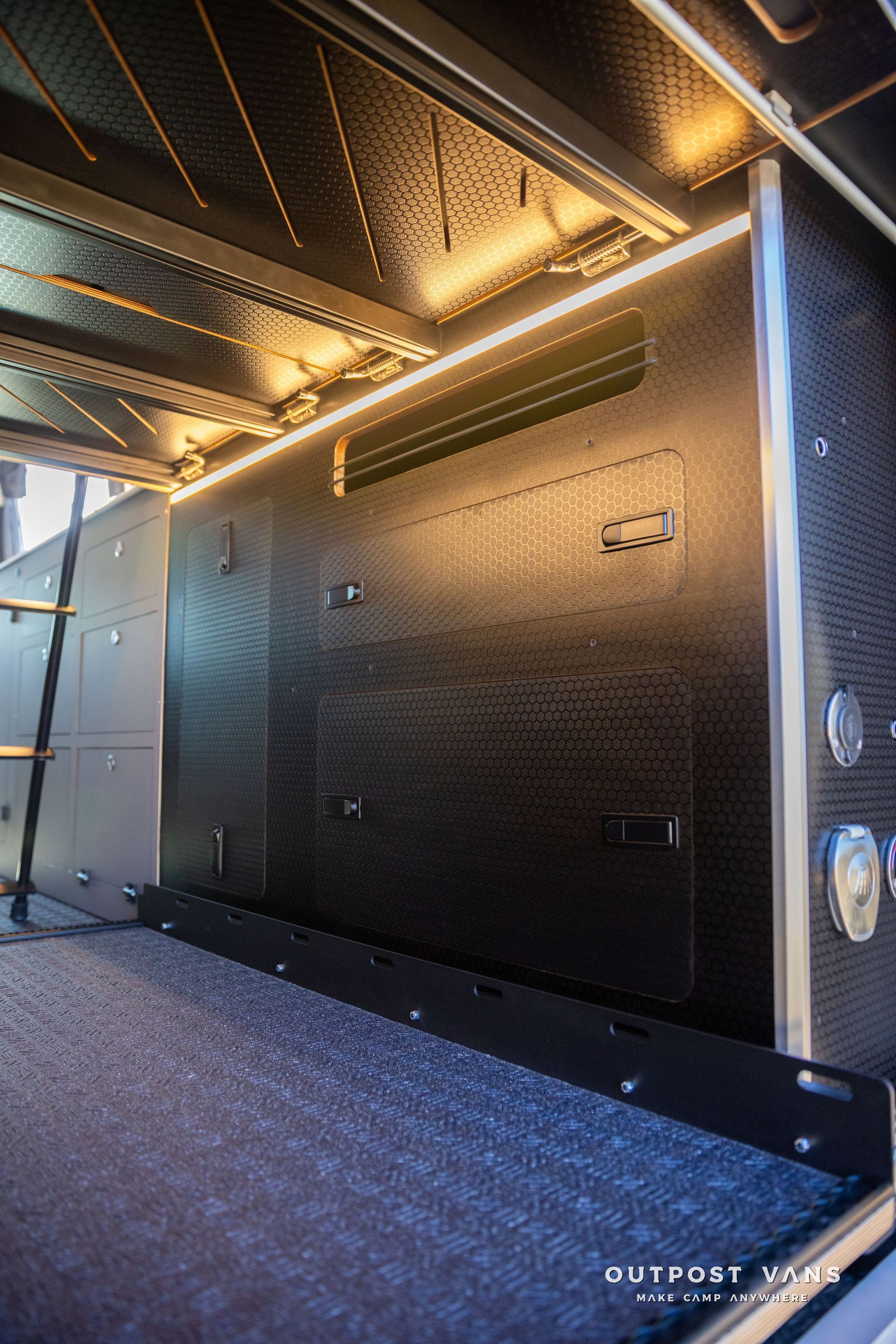 Interior view of a camper van with black paneling and overhead lighting.