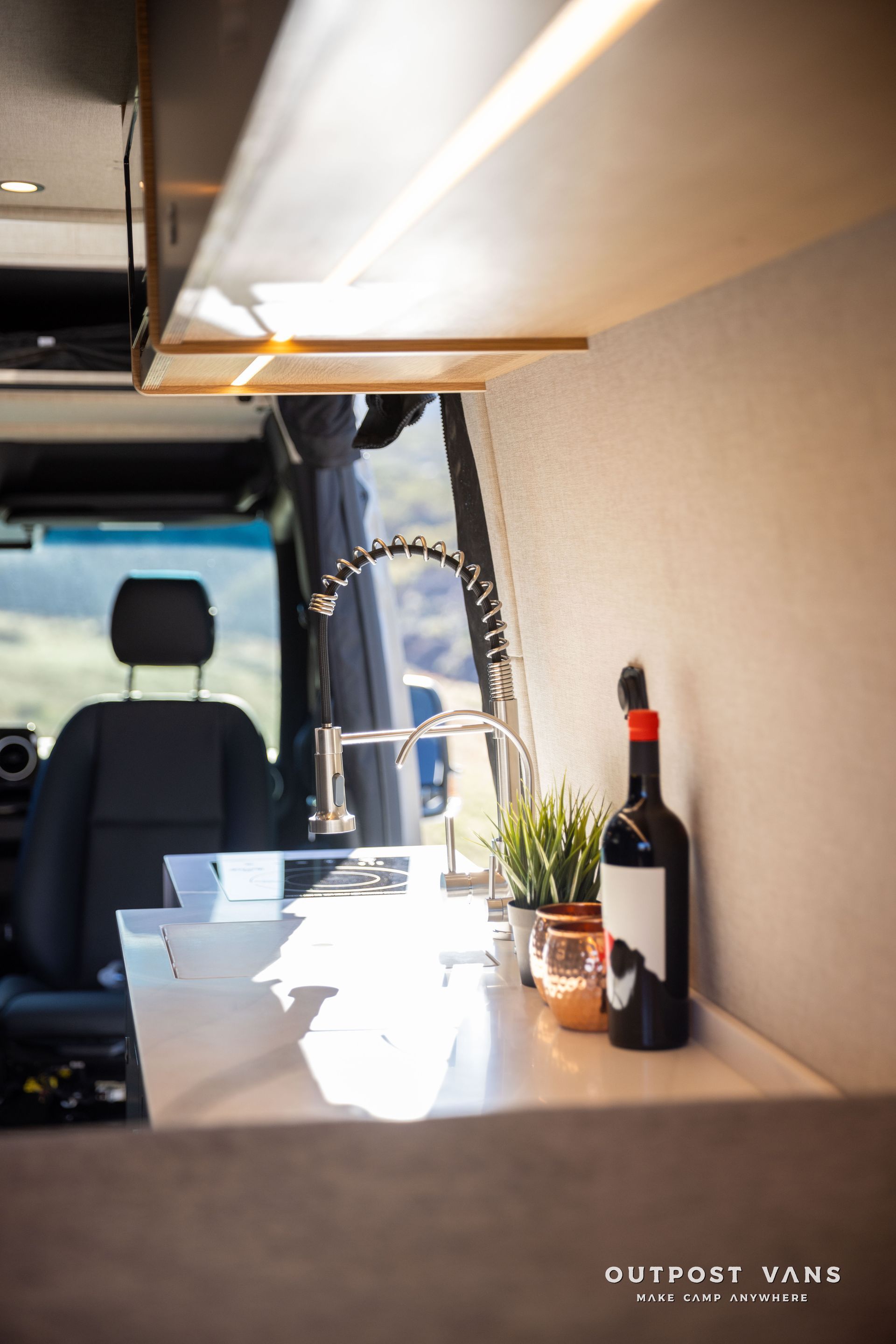 Interior view of a camper van kitchen with a sink, plant, and a bottle of wine.