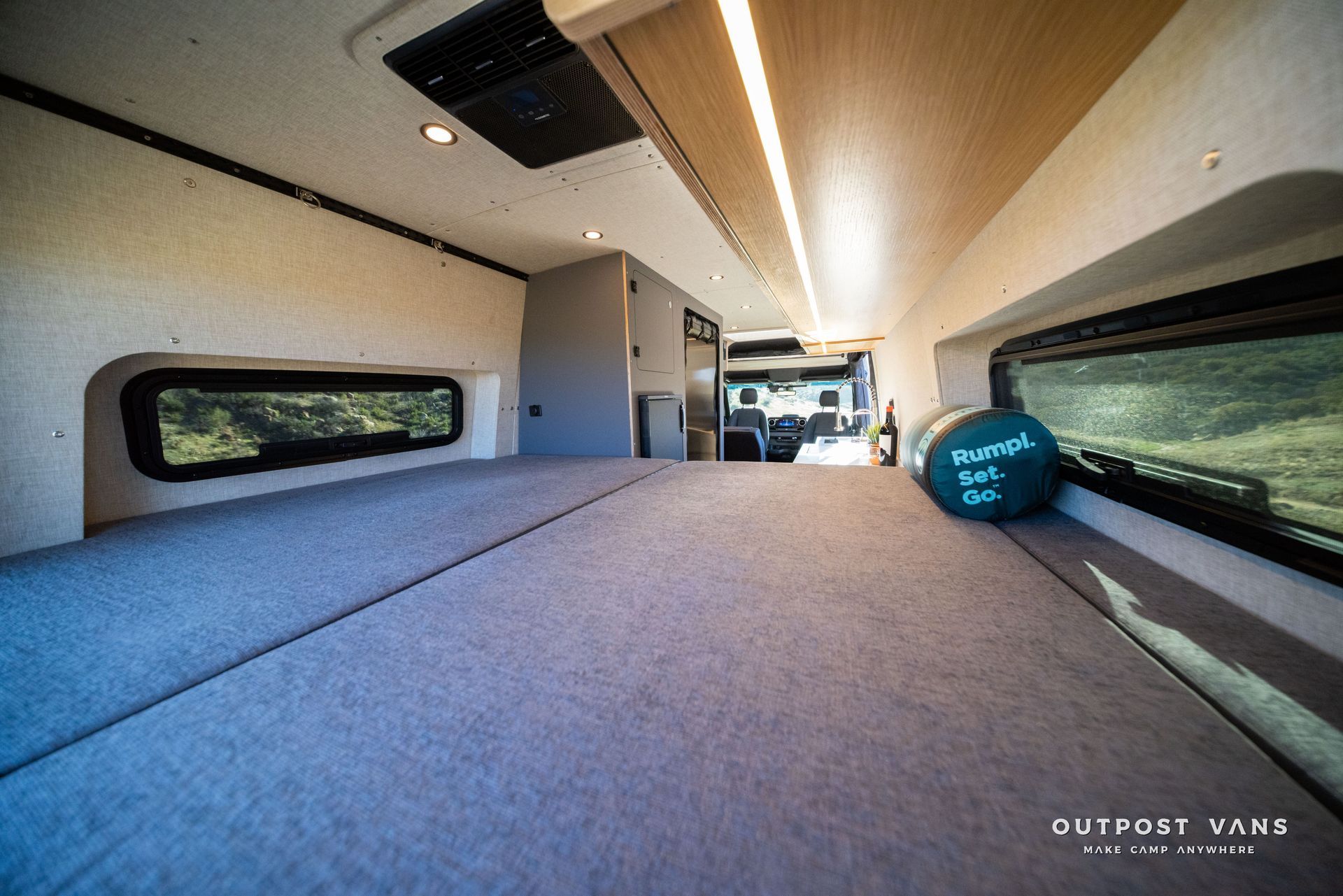 Interior of a camper van with a large bed, windows, and overhead storage.