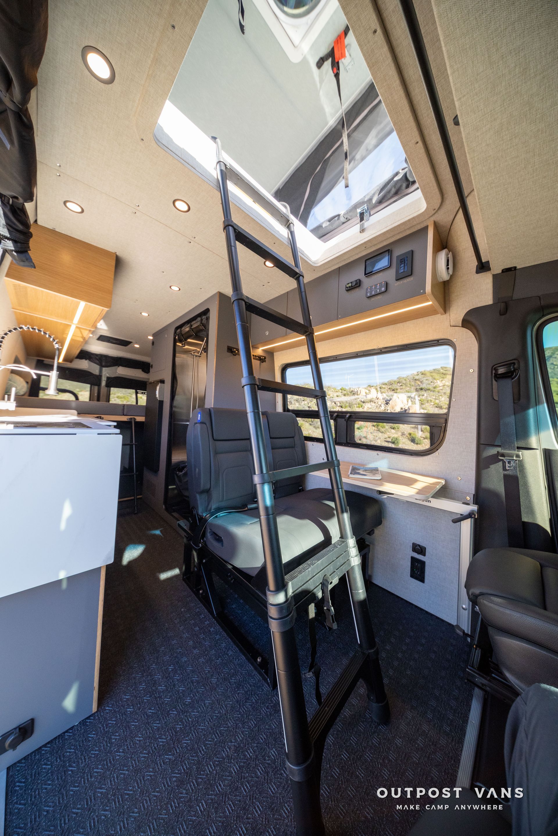 Interior of a camper van with a ladder to an upper sleeping area, skylight, and open windows.