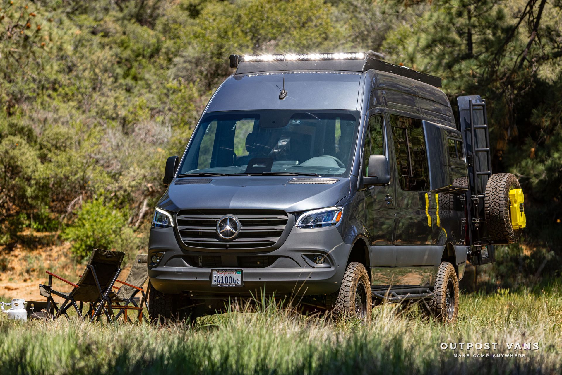 Grey Mercedes camper van parked in a grassy, wooded campsite