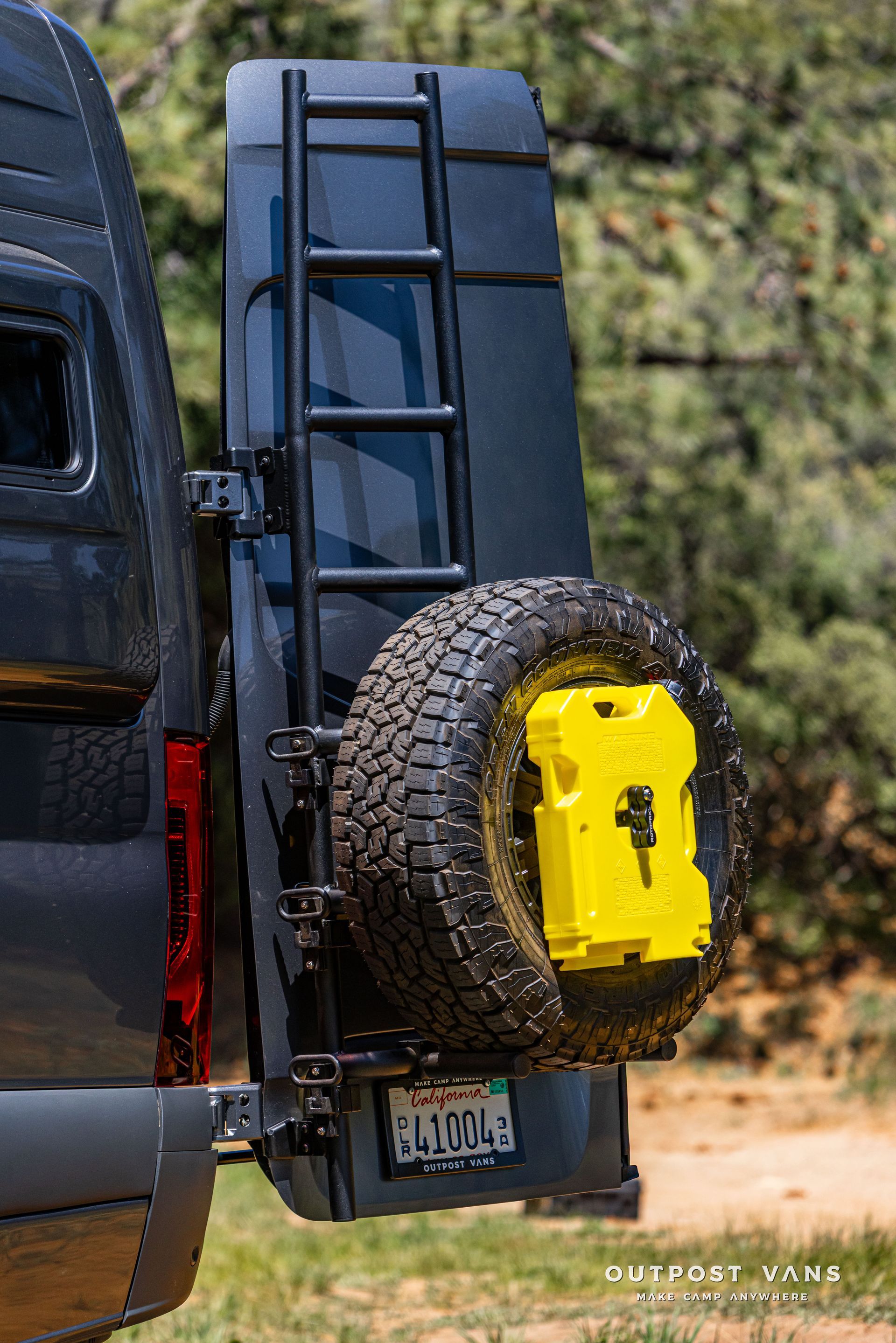 Black SUV with a rear-mounted spare tire featuring a bright yellow fuel can in a wooded area