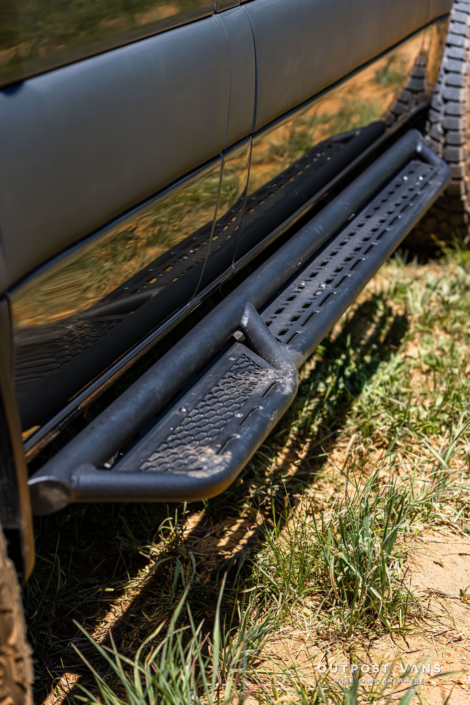 Black truck side step and running board beside grass, with rear tire visible.