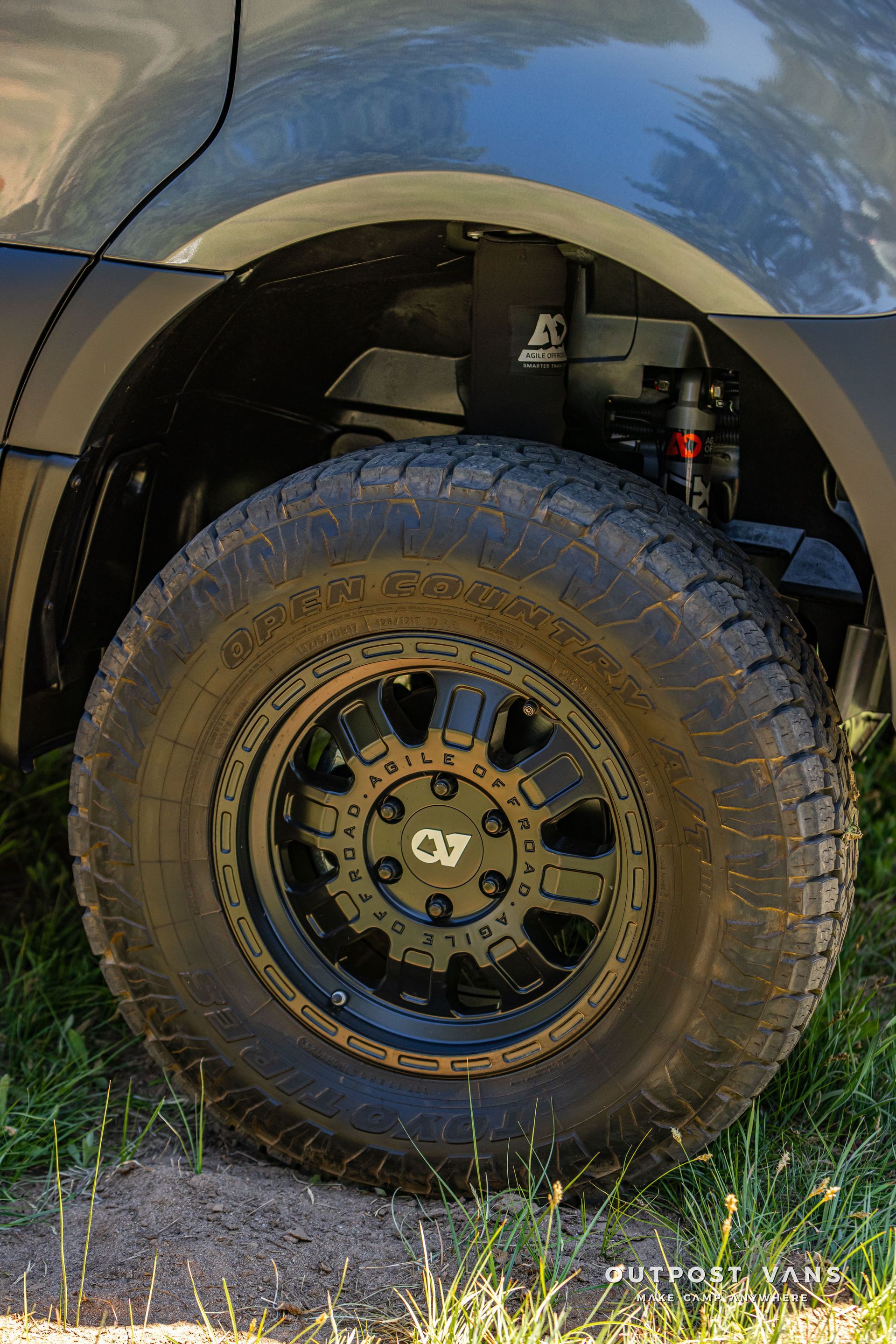Close-up of a truck’s rear wheel and wheel well with black tire and off-road rim under a dark fender.