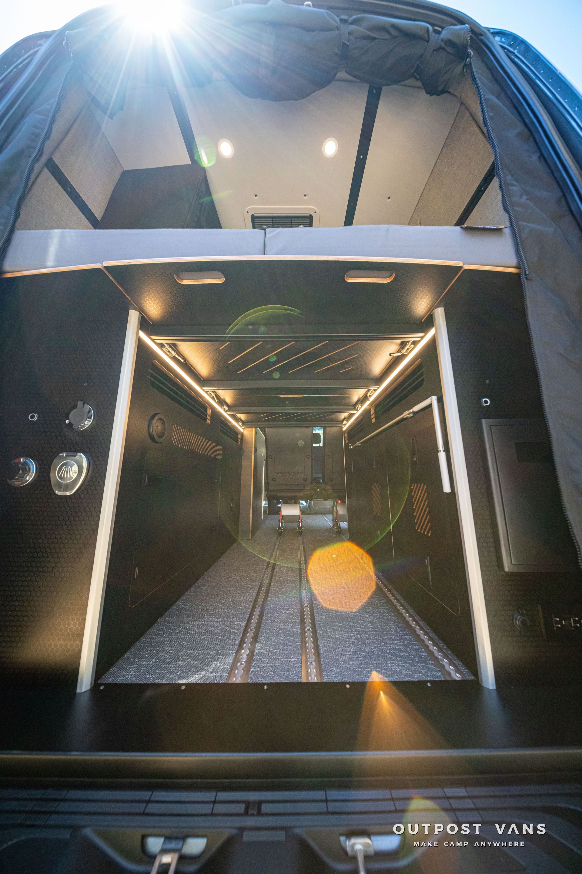 Open RV doorway showing a lit interior hallway with patterned floor and sun glare outside