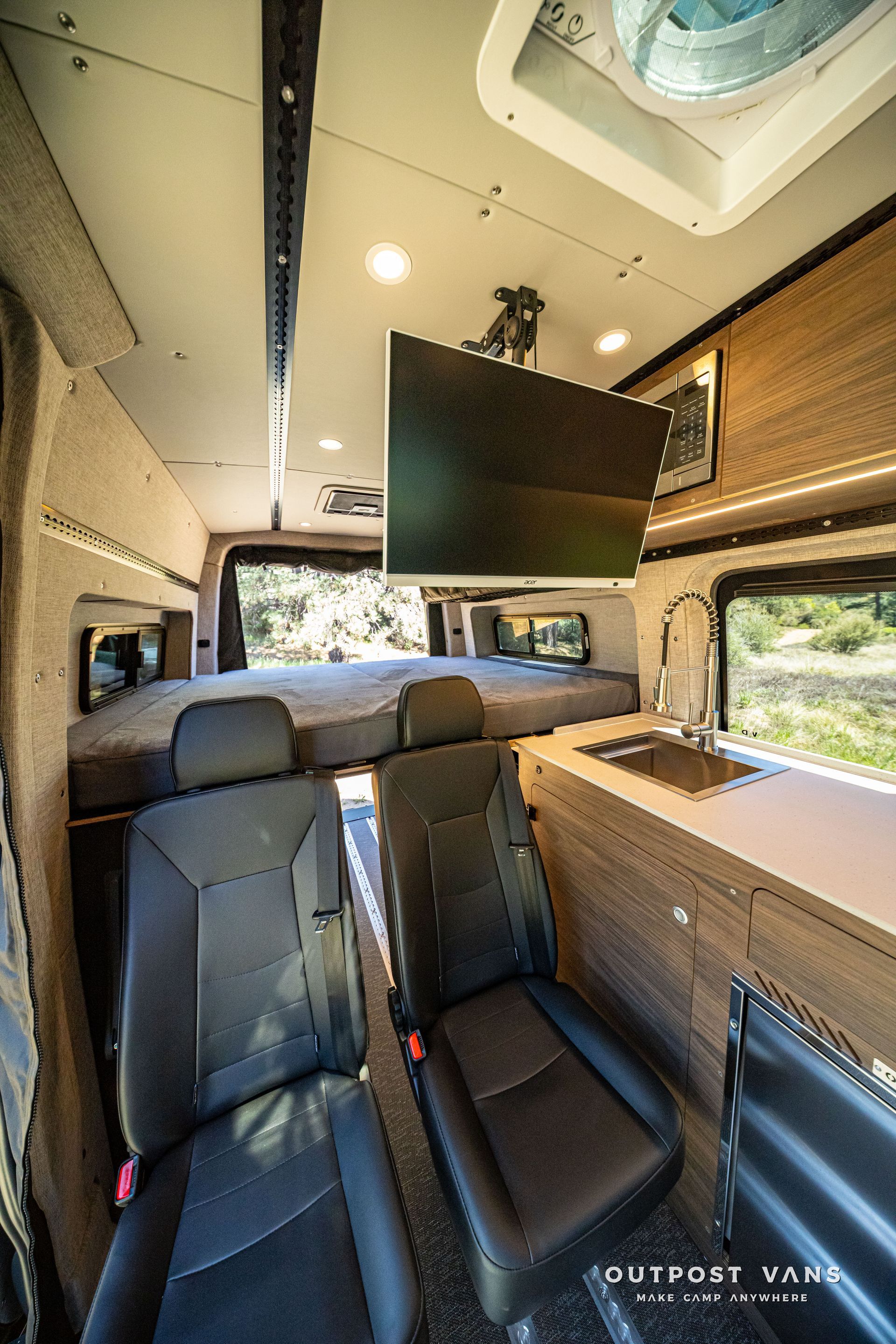 Camper van interior with front seats, bed, overhead cabinets, and a skylight window