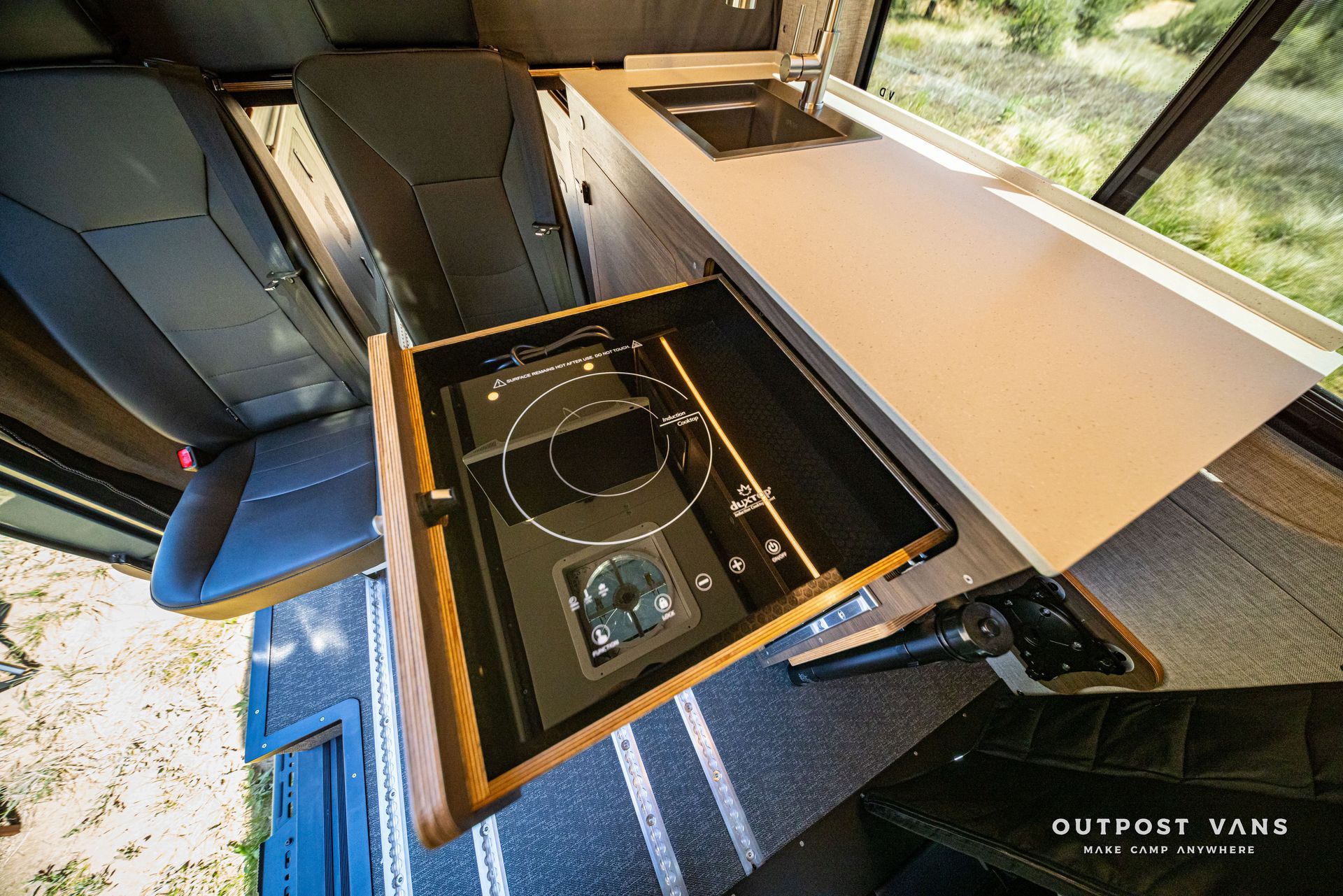 Overhead view of a camper van kitchen with a slide-out cooktop and sink beside a window.