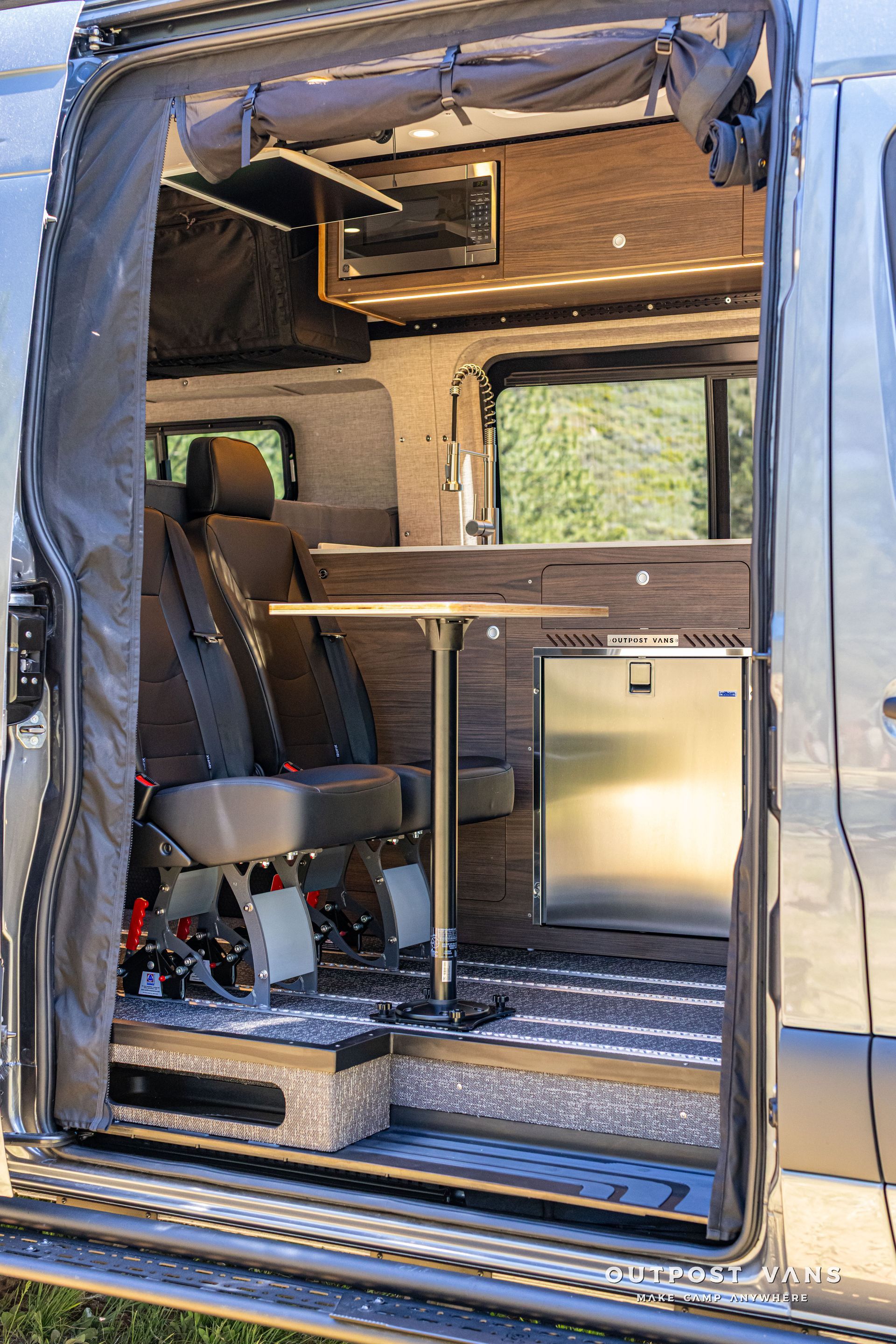 Open van interior with wood shelves, seat, and small stainless fridge in a camper conversion