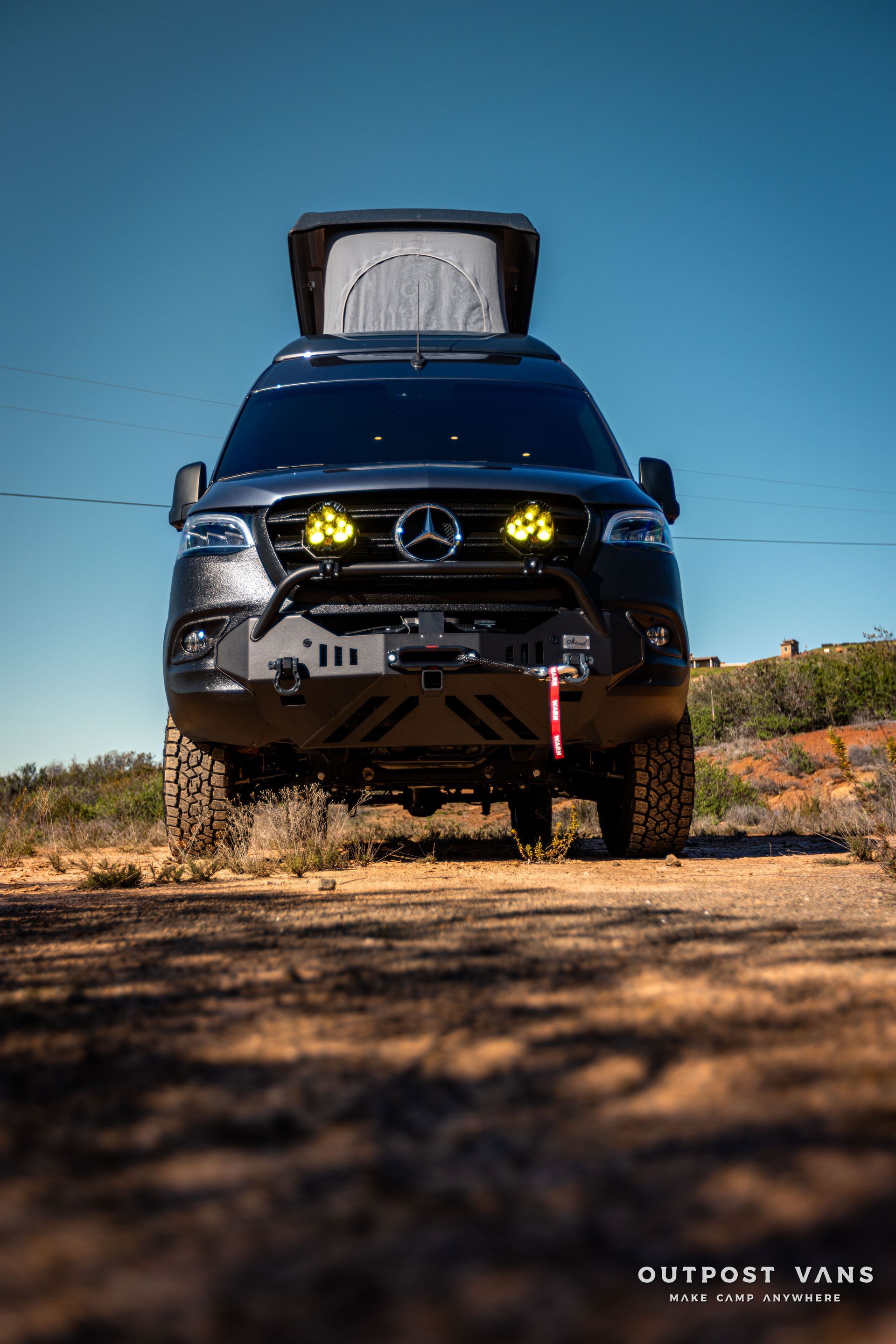 a mercedes sprinter van is parked on the side of a dirt road .