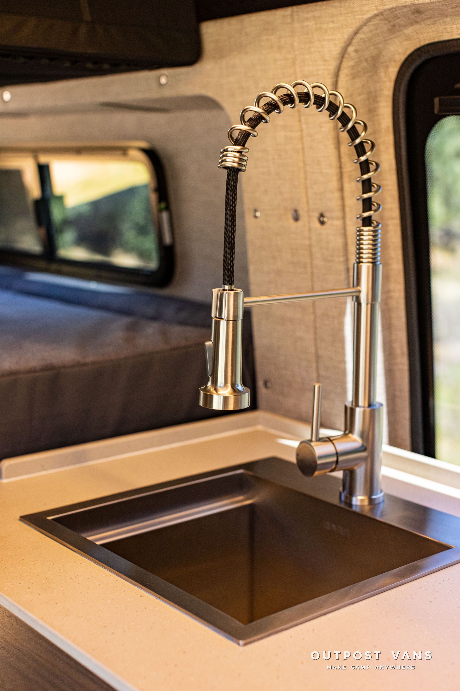 Stainless-steel sink with tall spring-coil faucet inside an RV kitchen counter.