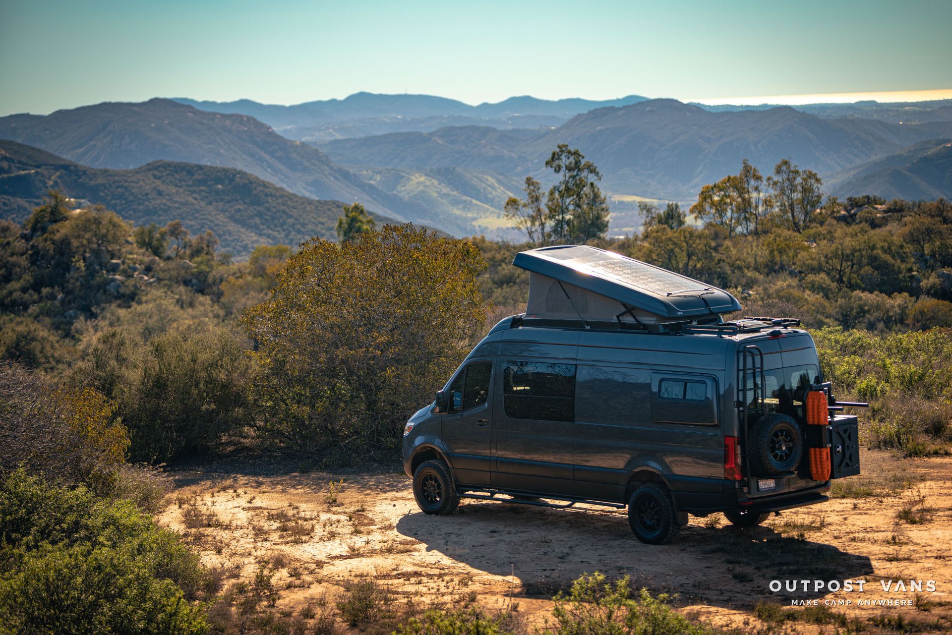 a van is parked on top of a dirt hill with mountains in the background .