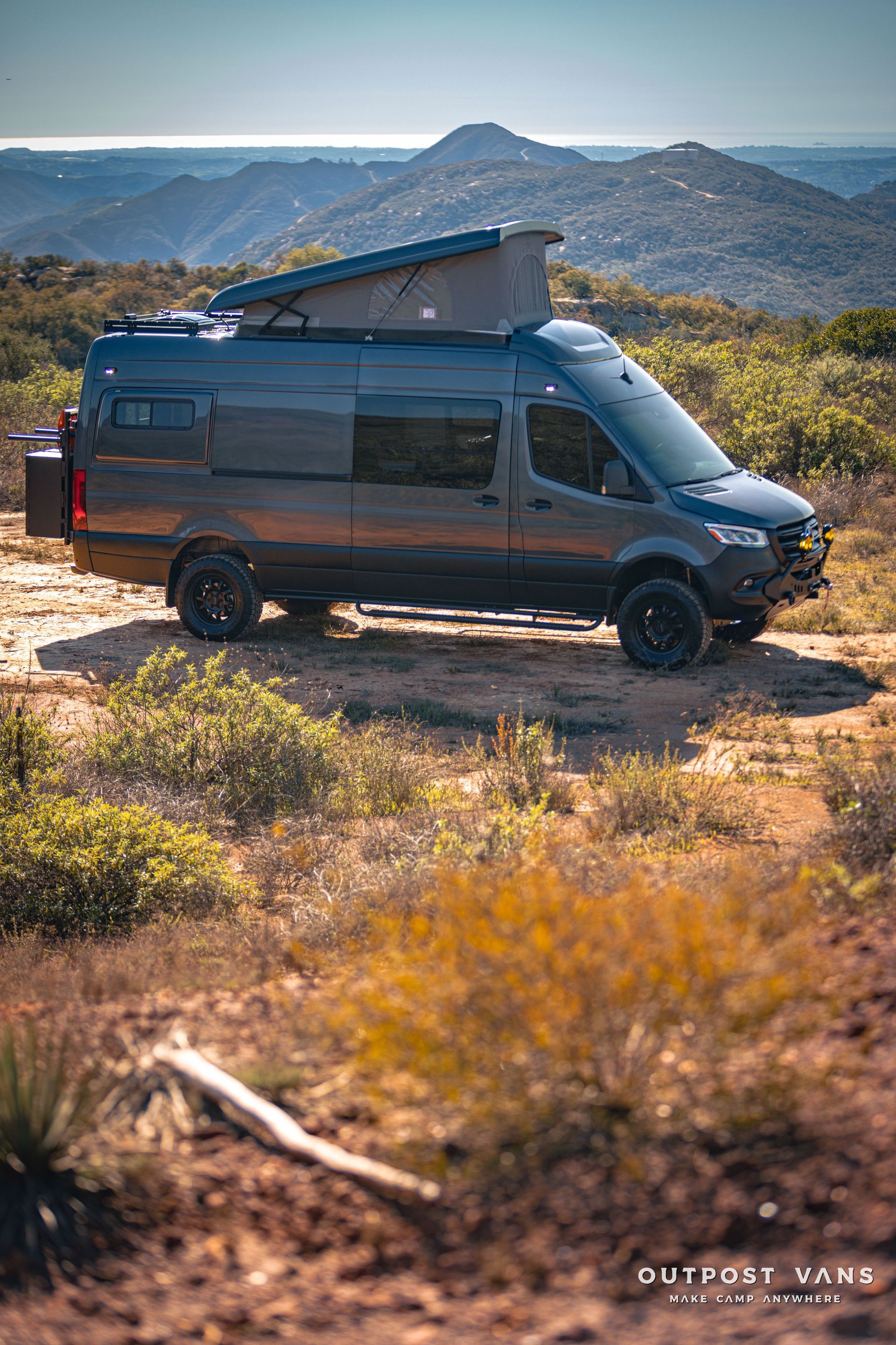 a van is parked on top of a dirt hill with mountains in the background .
