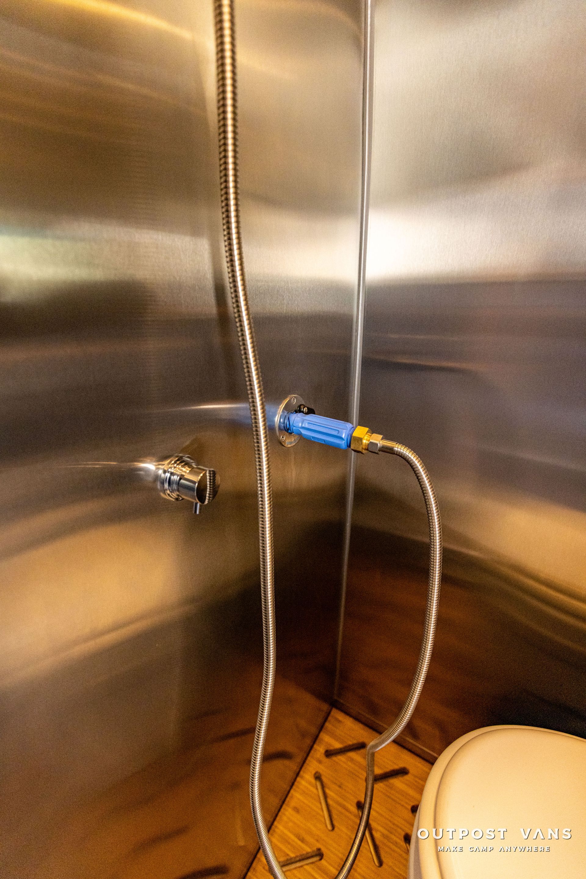 a shower head is attached to a stainless steel wall next to a toilet .