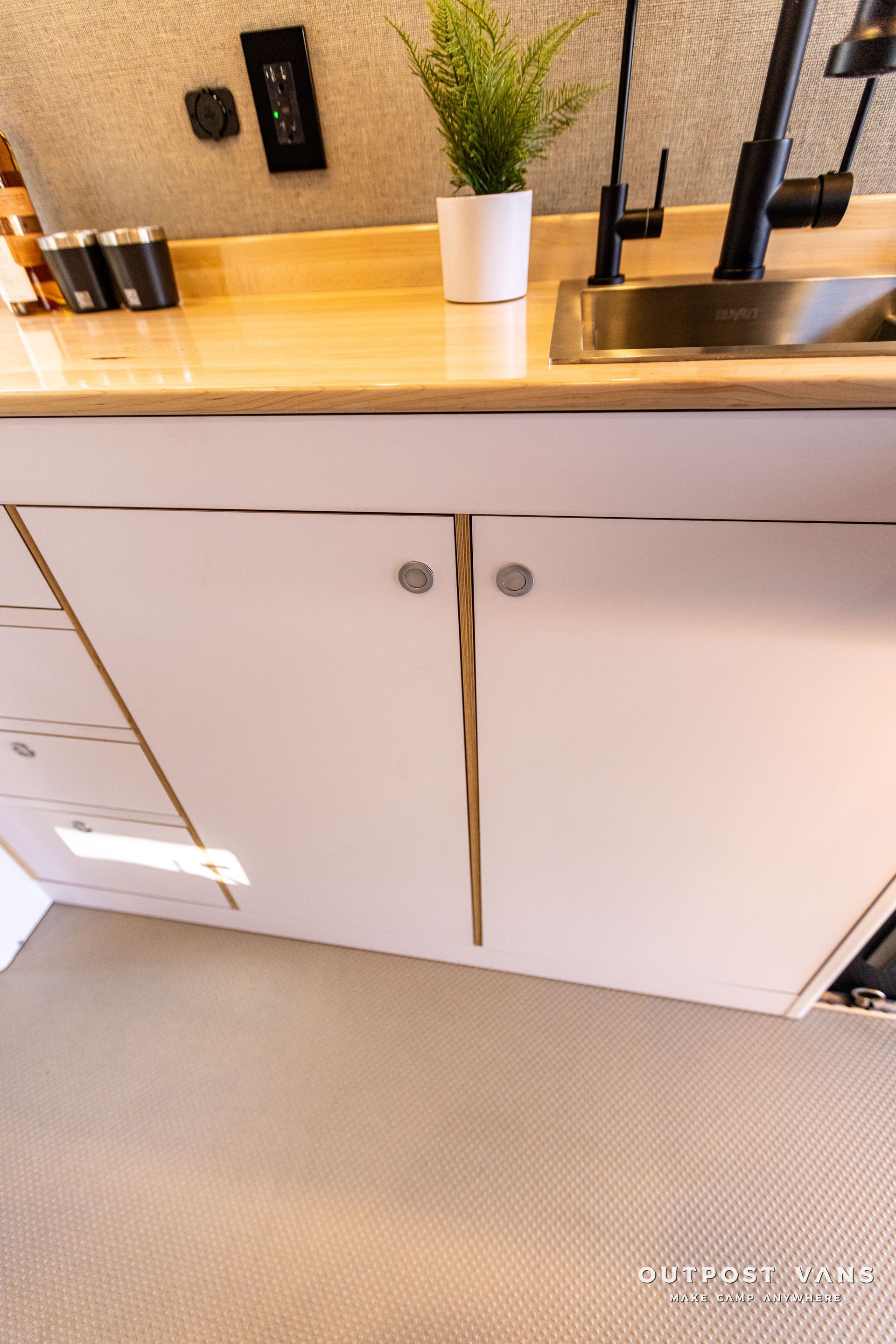 a kitchen with a sink , cabinets , drawers and a potted plant on the counter .