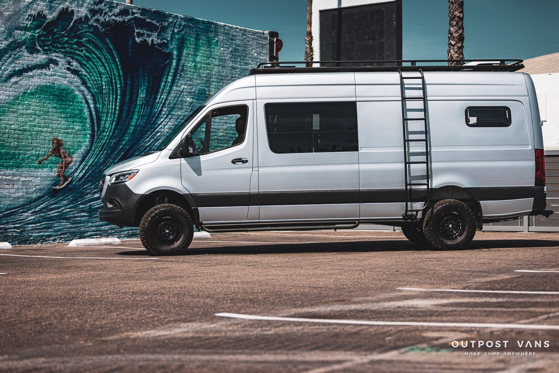 a white van with a ladder on the roof is parked in a parking lot .