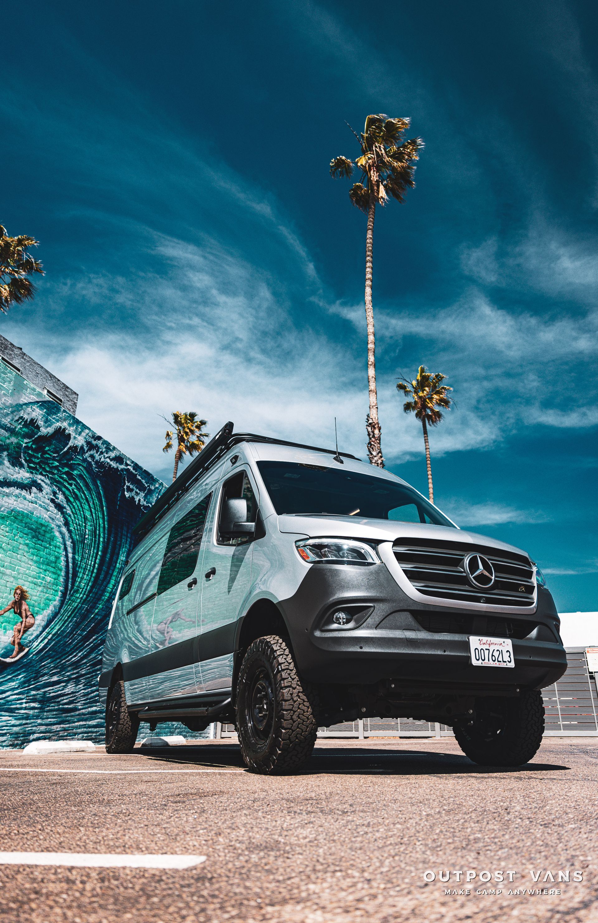 a van is parked in a parking lot in front of a mural of a wave .