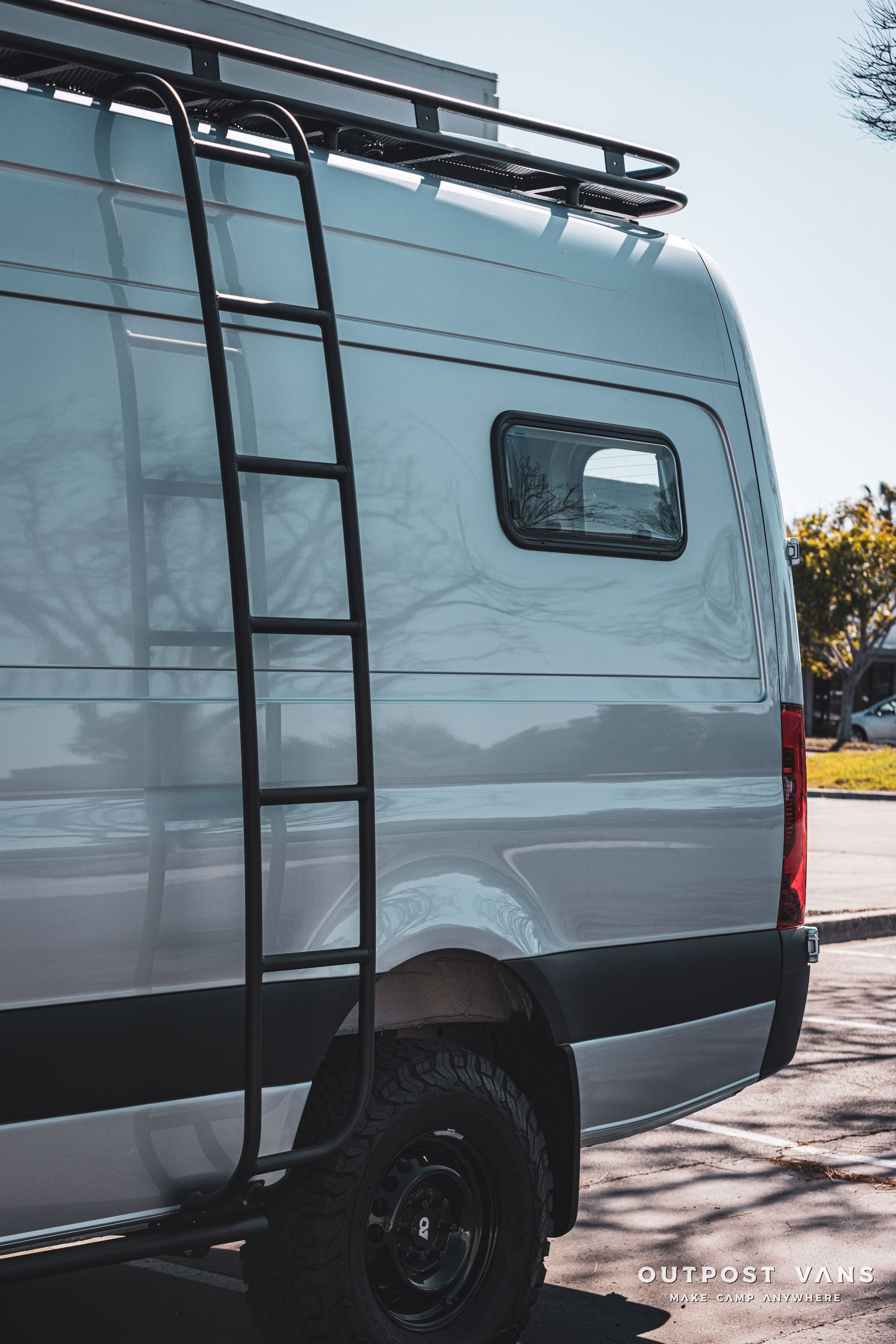 a white van with a ladder on the back is parked in a parking lot .