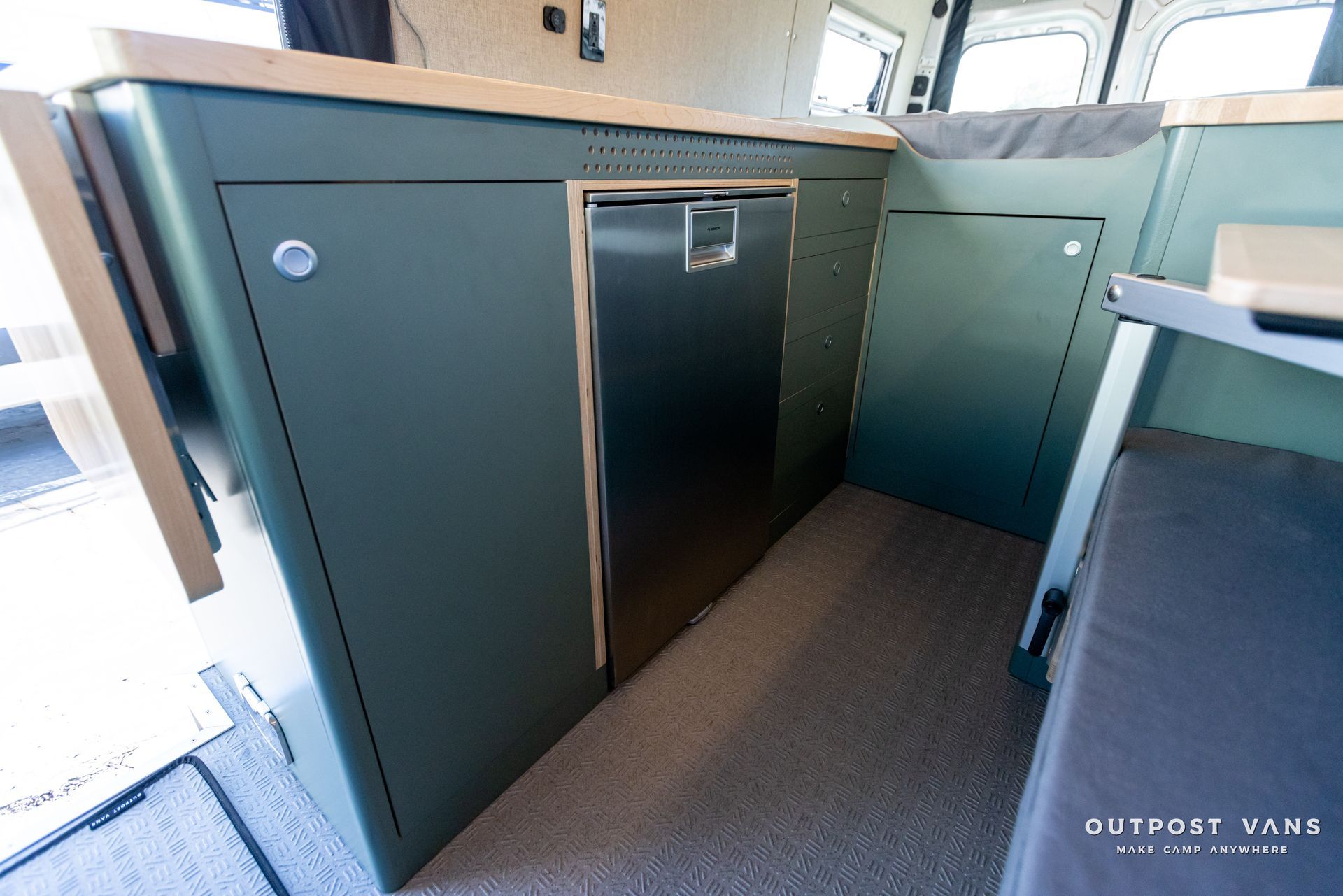a camper van with green cabinets and a stainless steel dishwasher .