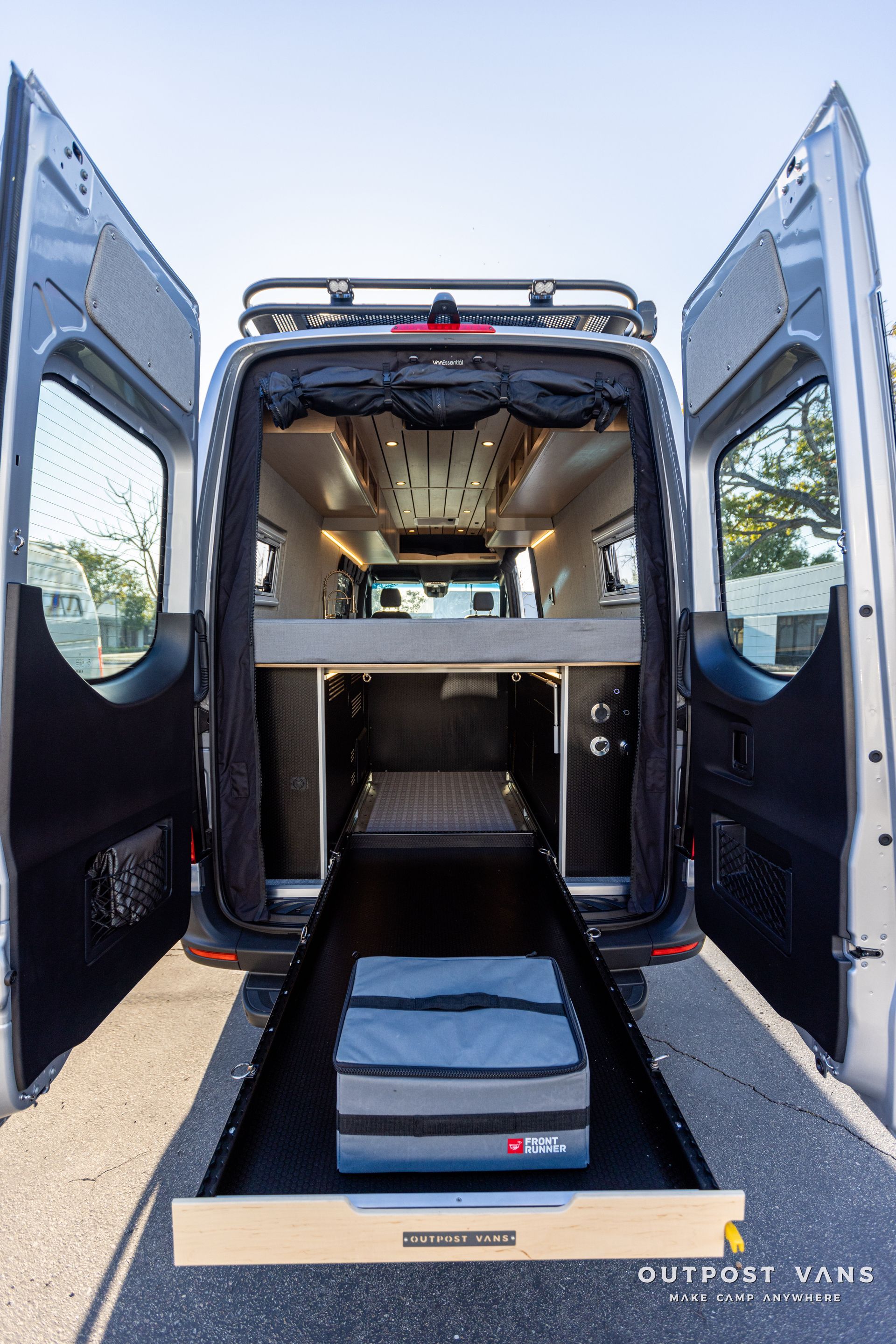 the back of a van with its doors open and a bed in the back .