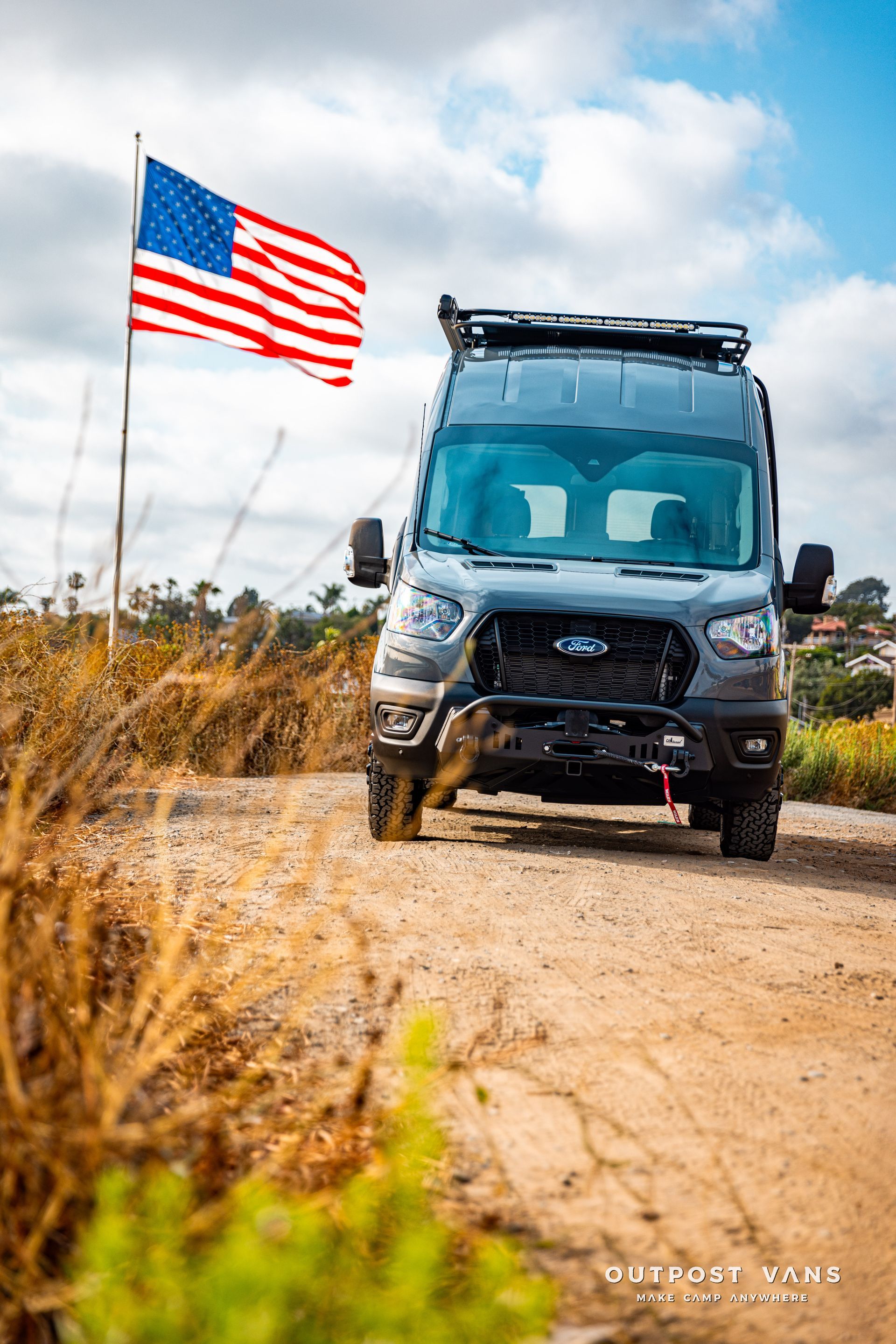 a van is parked on a dirt road next to an american flag .