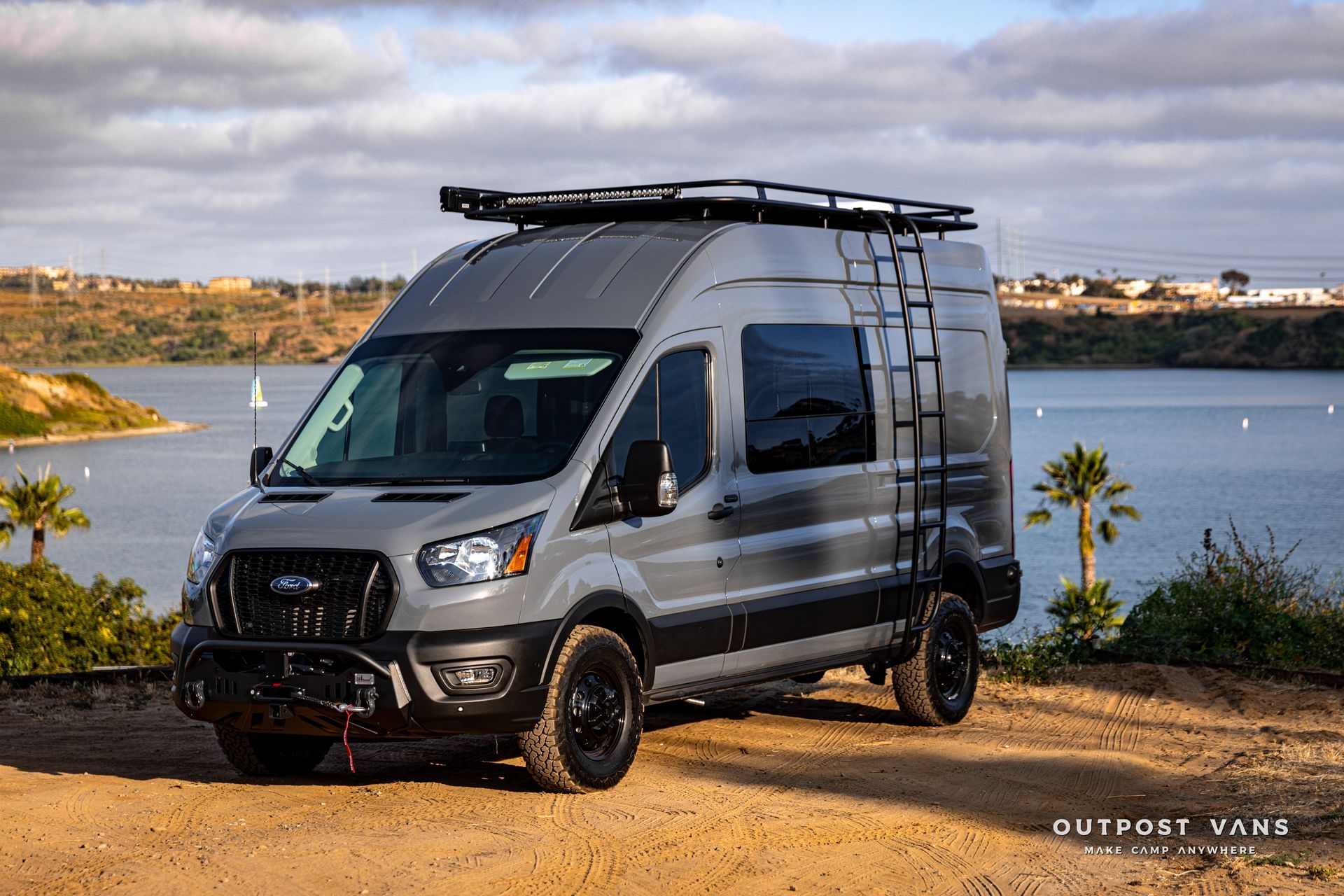 a van is parked on a dirt road next to a body of water .