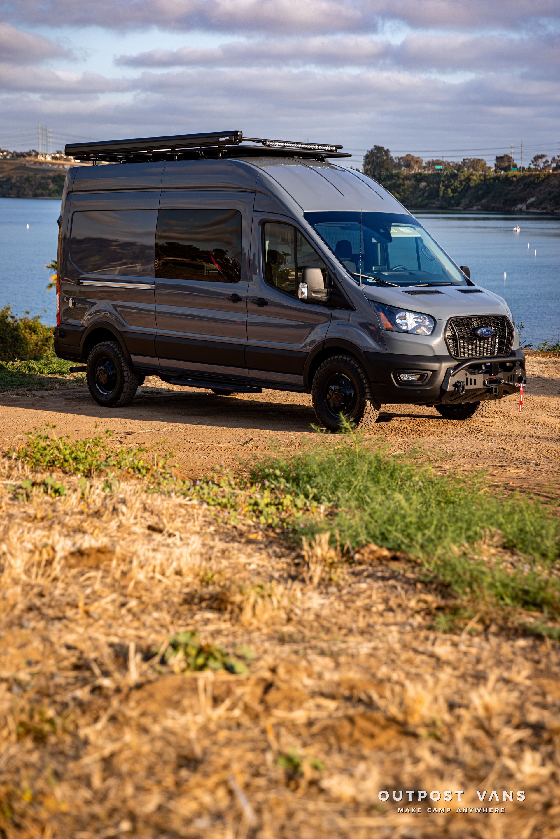 a van is parked on a dirt road next to a body of water .