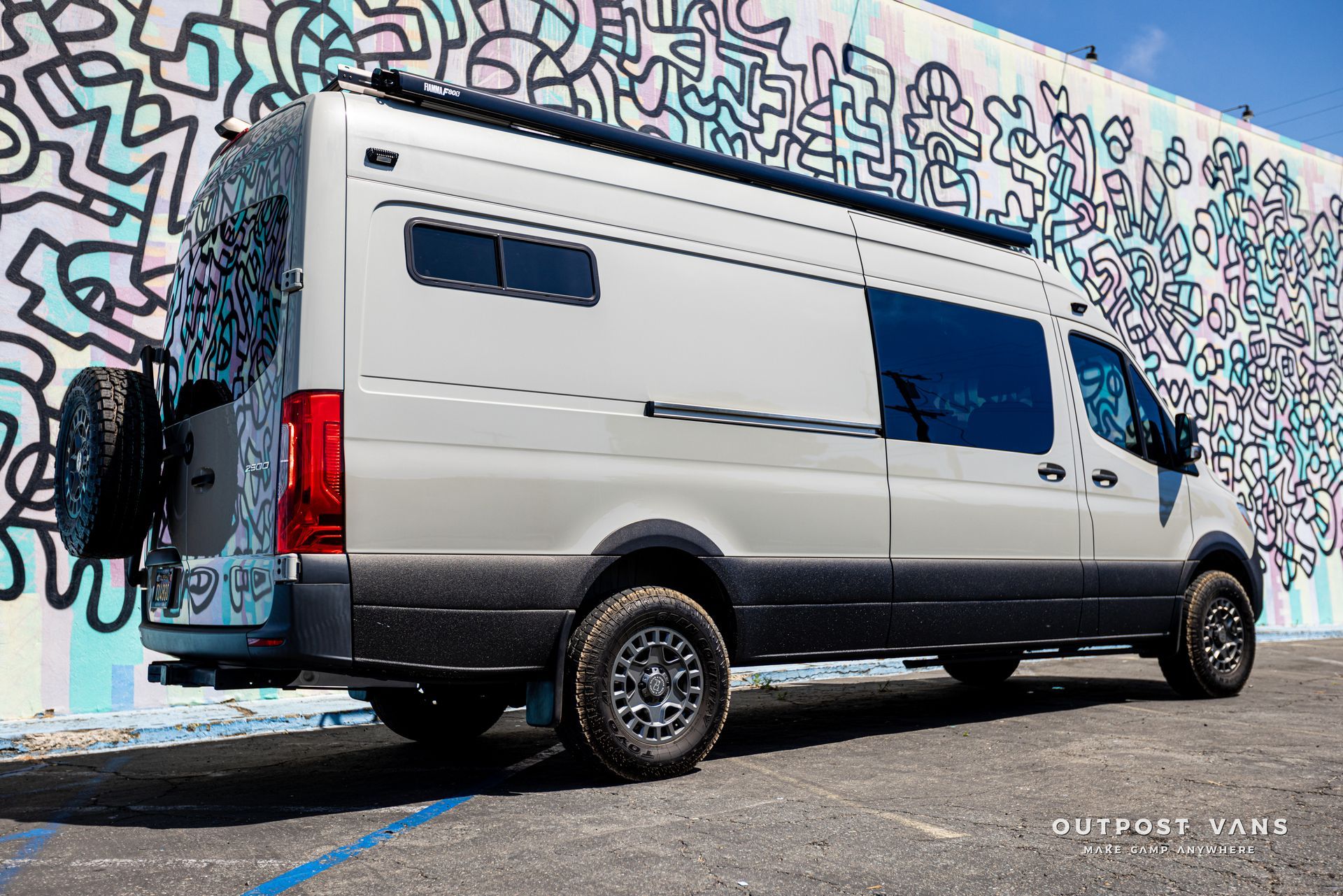 A white van is parked in front of a graffiti covered wall.