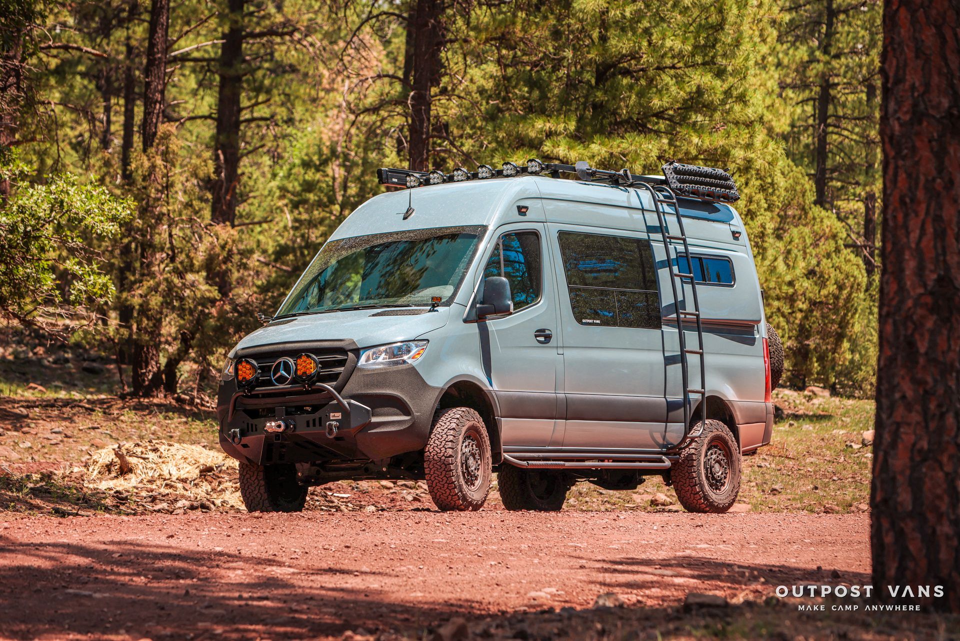a van with a ladder on the roof is parked on a dirt road in the woods .