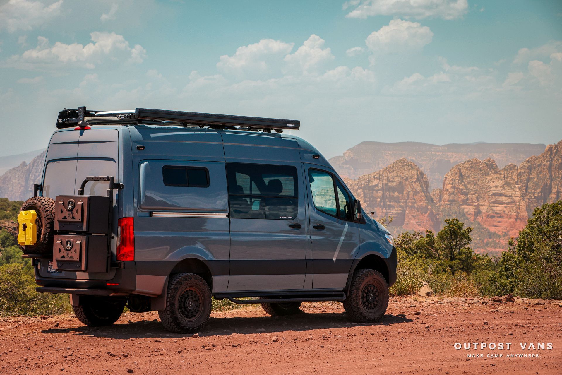 a gray van is parked in the middle of a dirt field with mountains in the background .