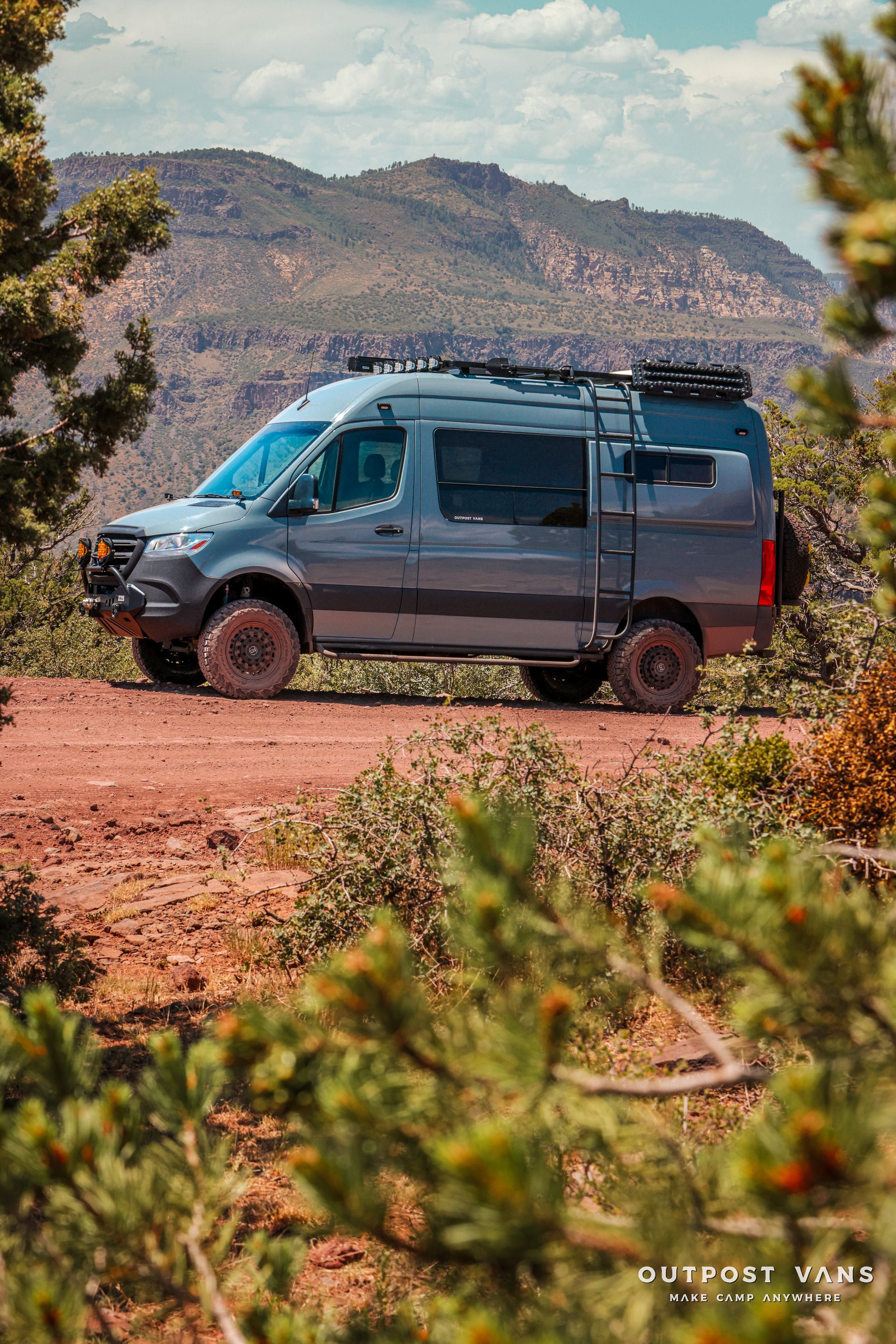 a van is parked on a dirt road with mountains in the background .