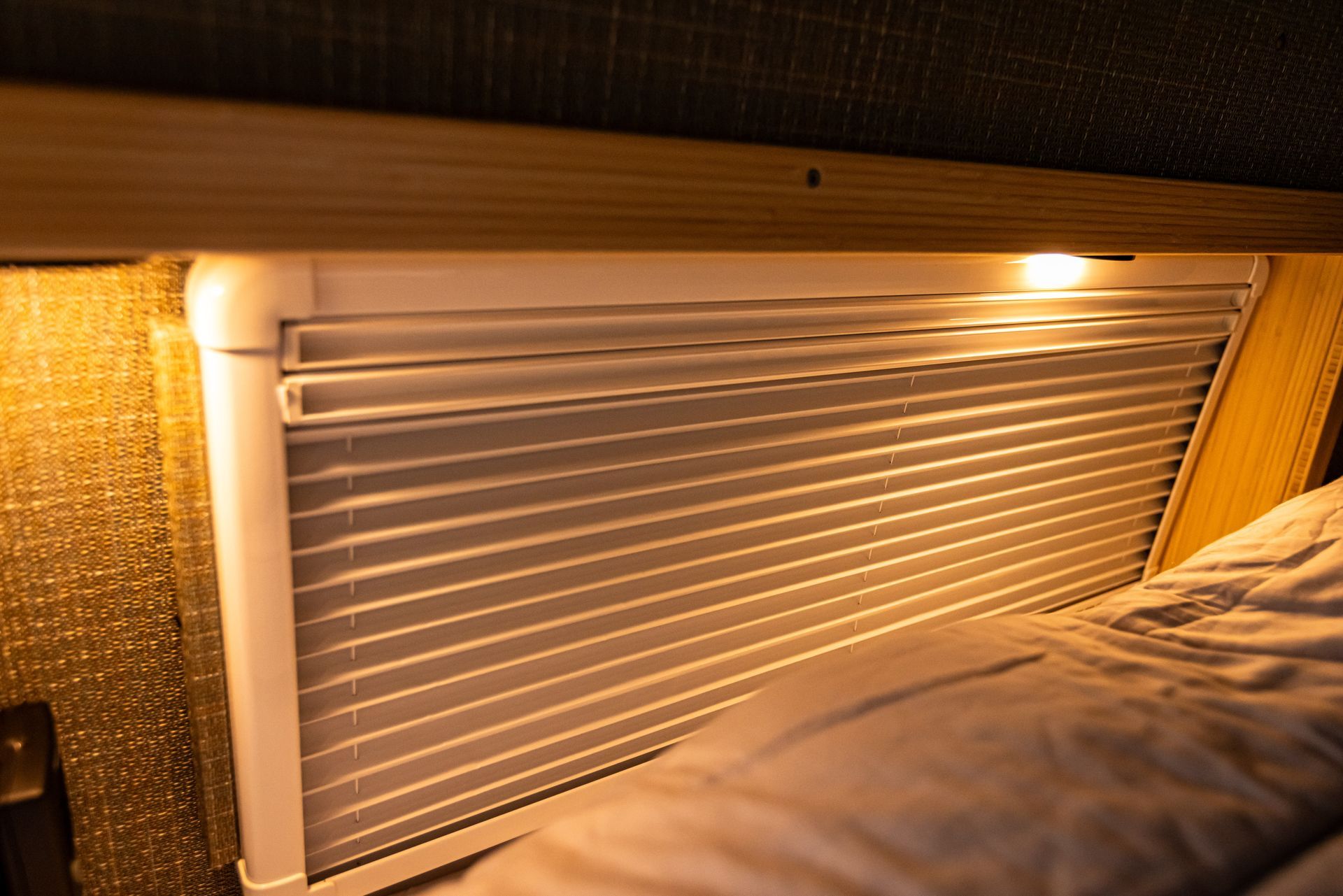 There is a light on the side of the bed next to a window.