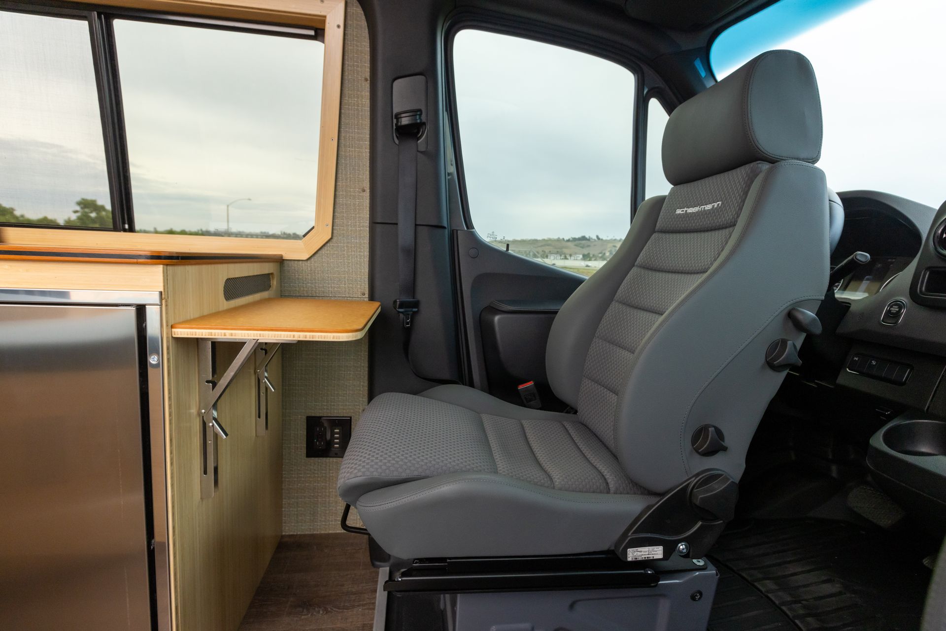 The inside of a van with a gray seat and a stainless steel refrigerator.