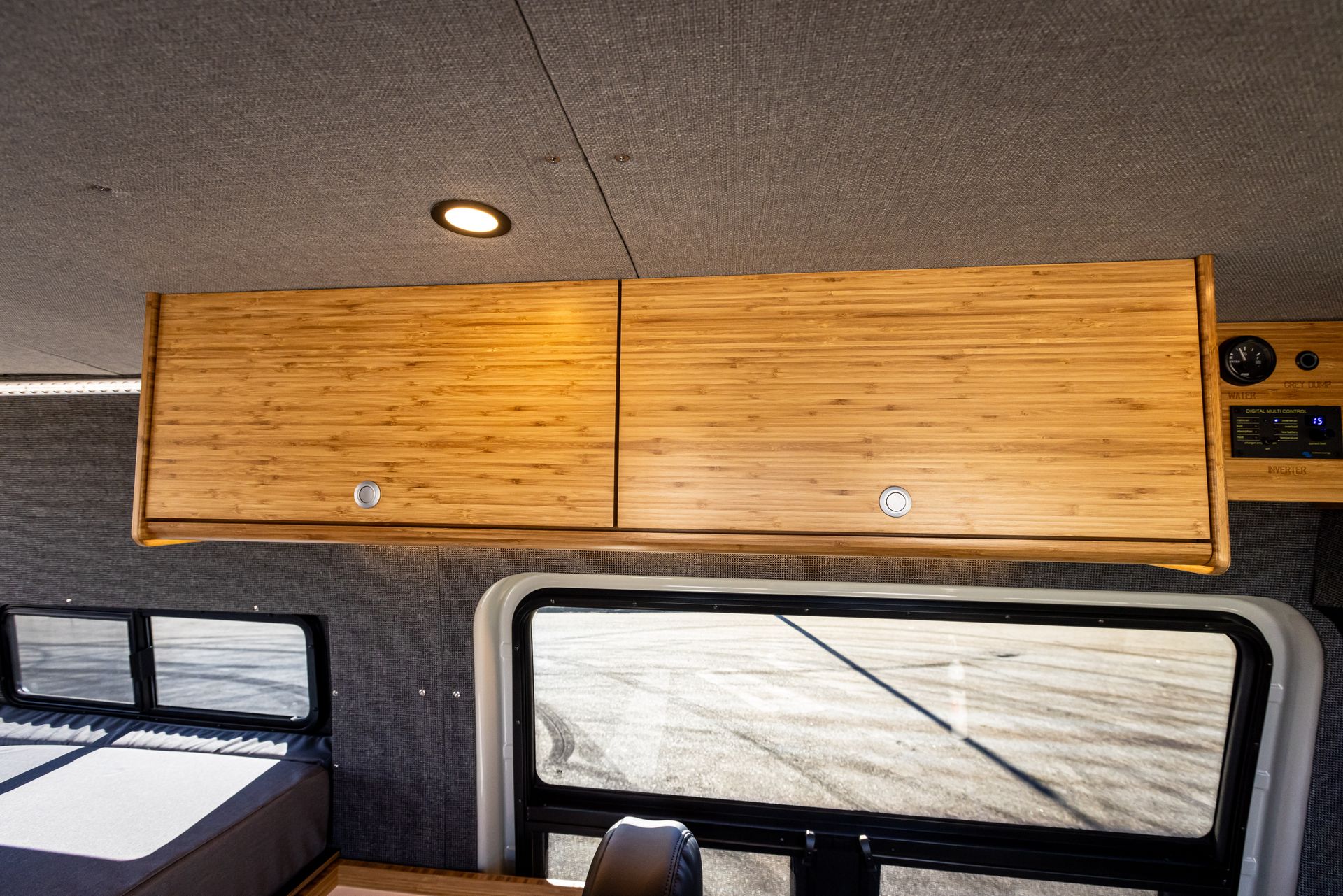 A van with a wooden cabinet above the bed and a window.