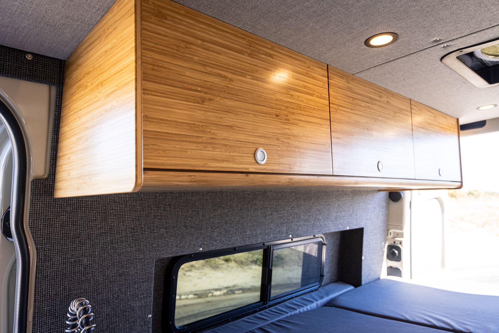 A van with a bed and wooden cabinets on the ceiling.