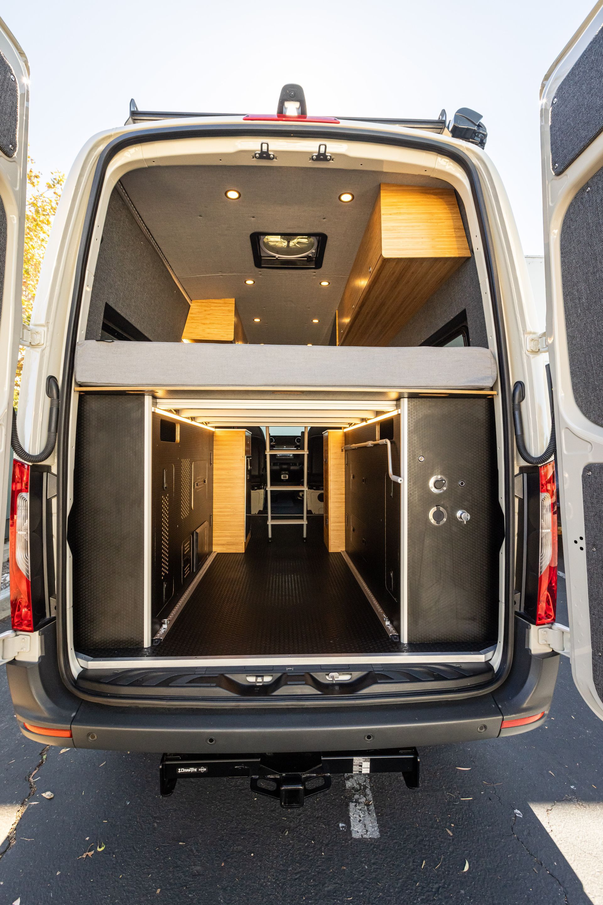 the back of a van with its doors open and a bed in the back .