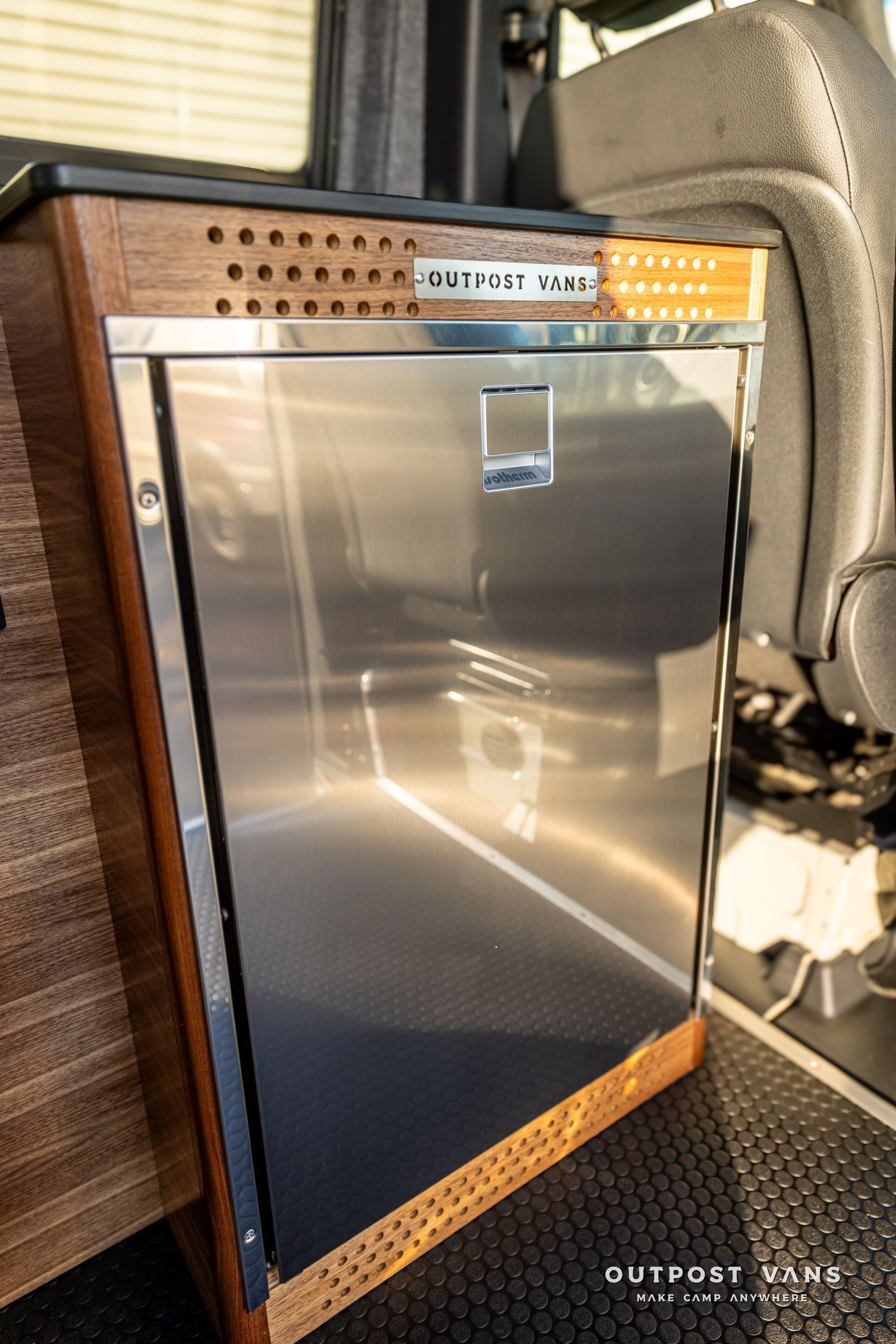 a stainless steel refrigerator is sitting next to a chair in a van .