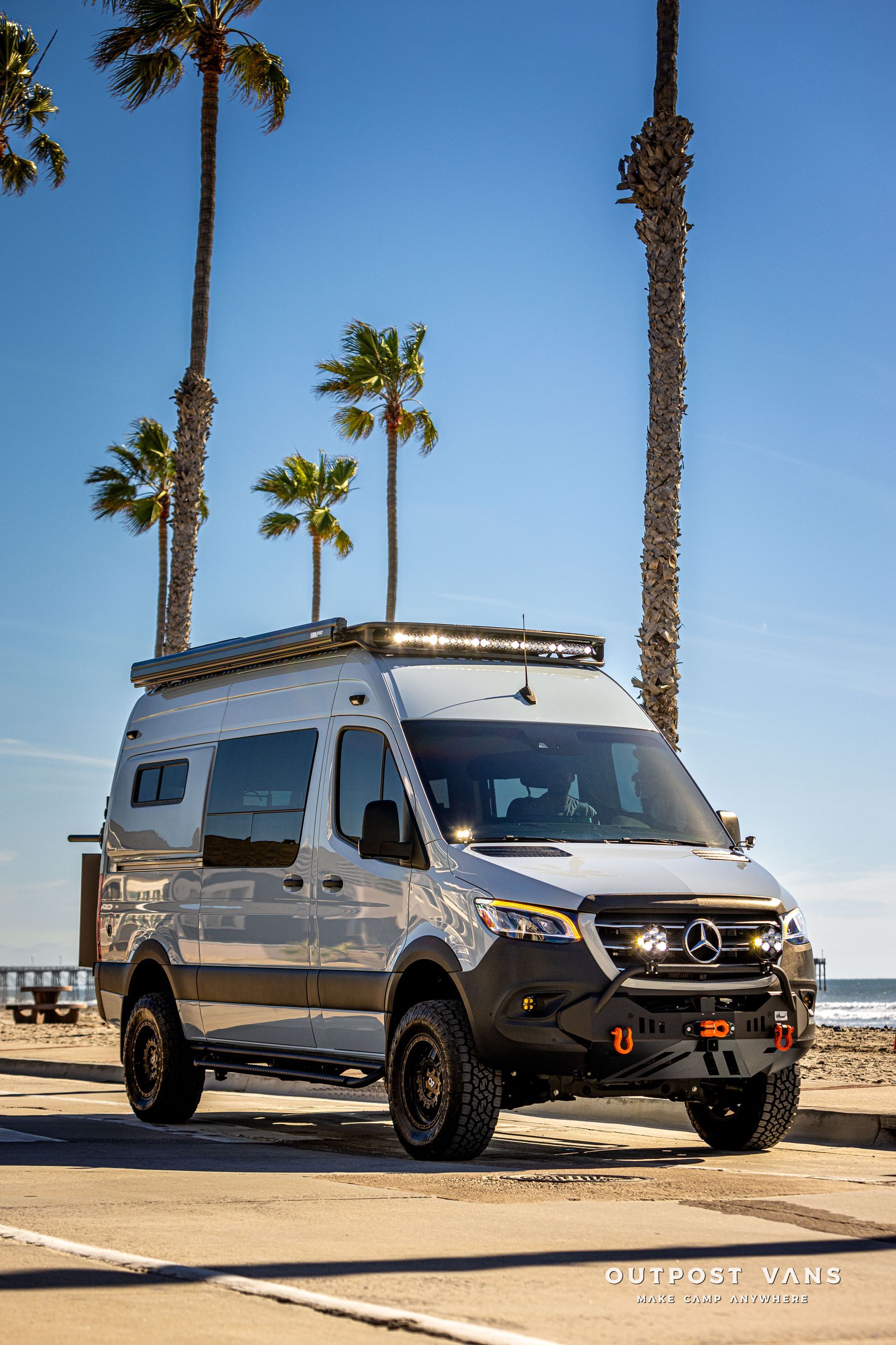 a white van is parked in a parking lot next to palm trees .