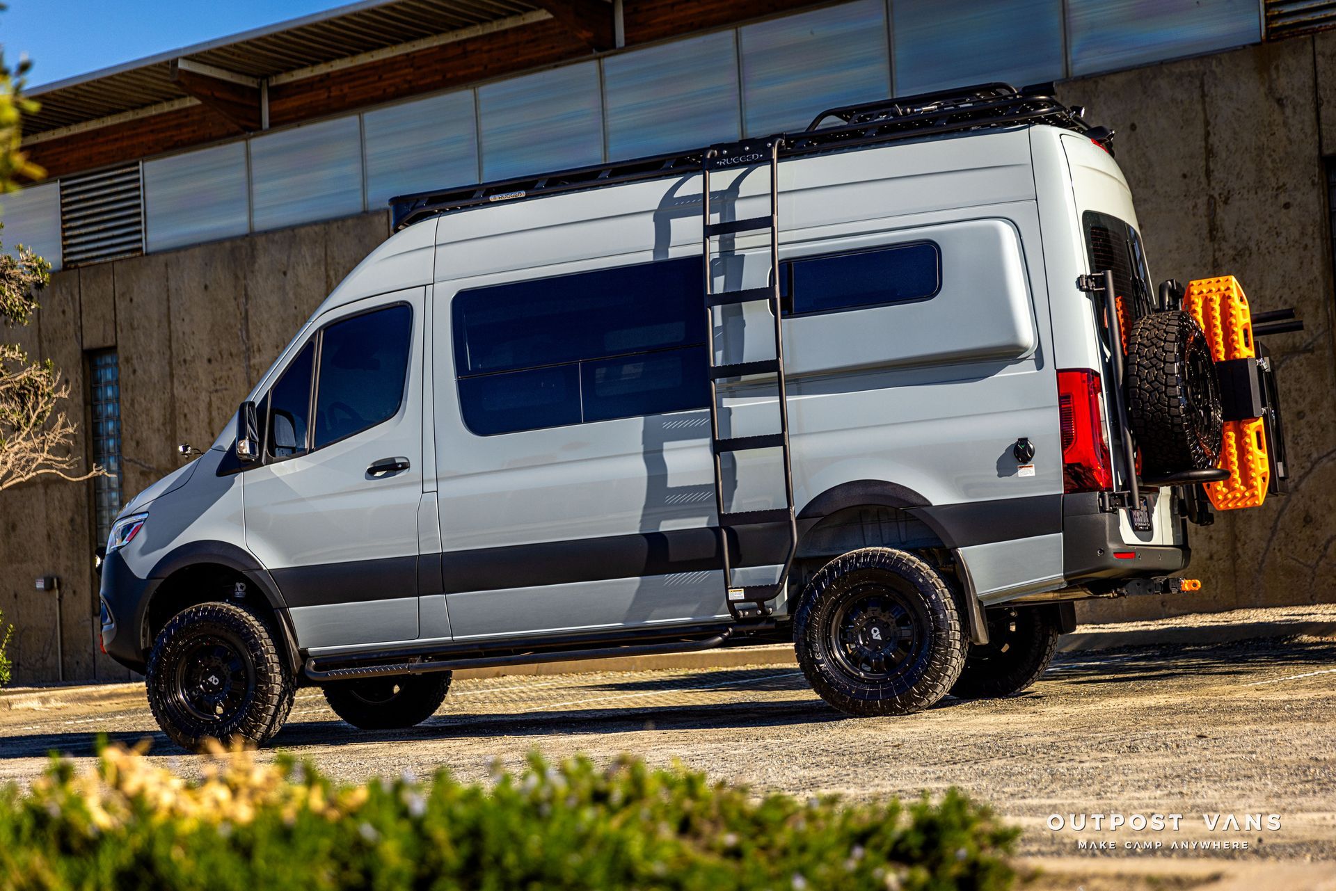 a white van with a ladder on the roof is parked in front of a building .