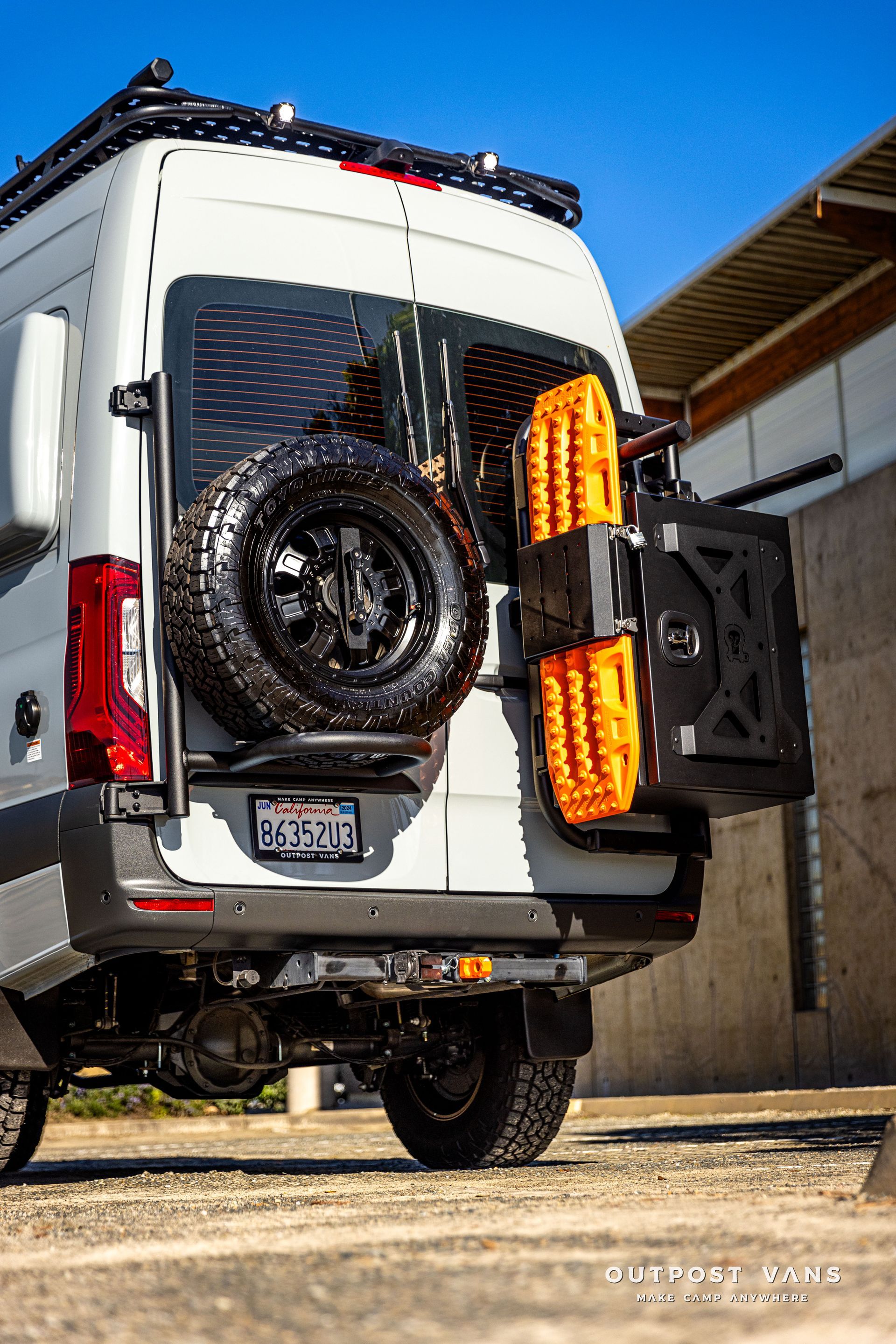 a white van with a spare tire on the back is parked in a parking lot .