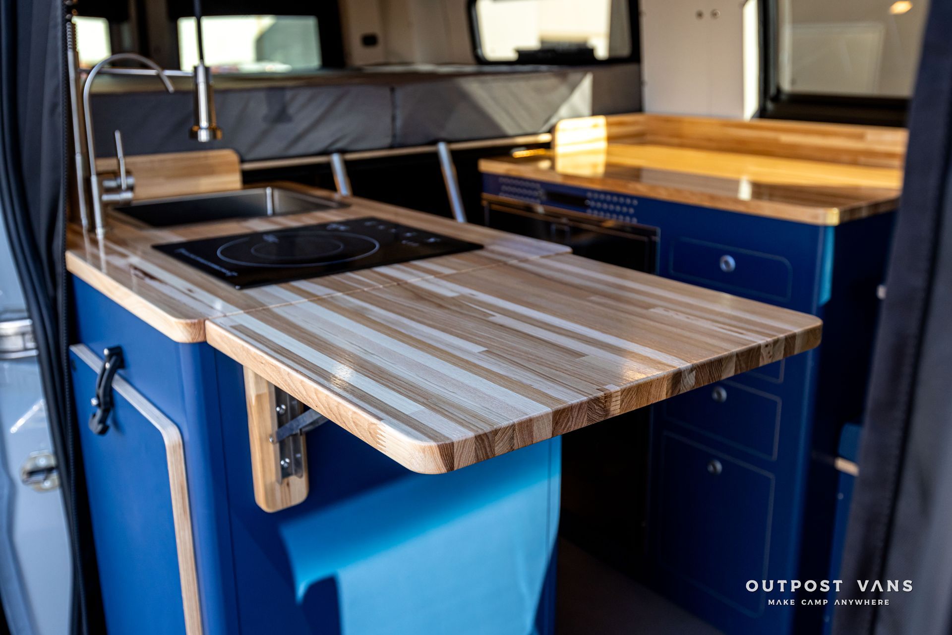 A kitchen in a van with a wooden counter top and a sink.