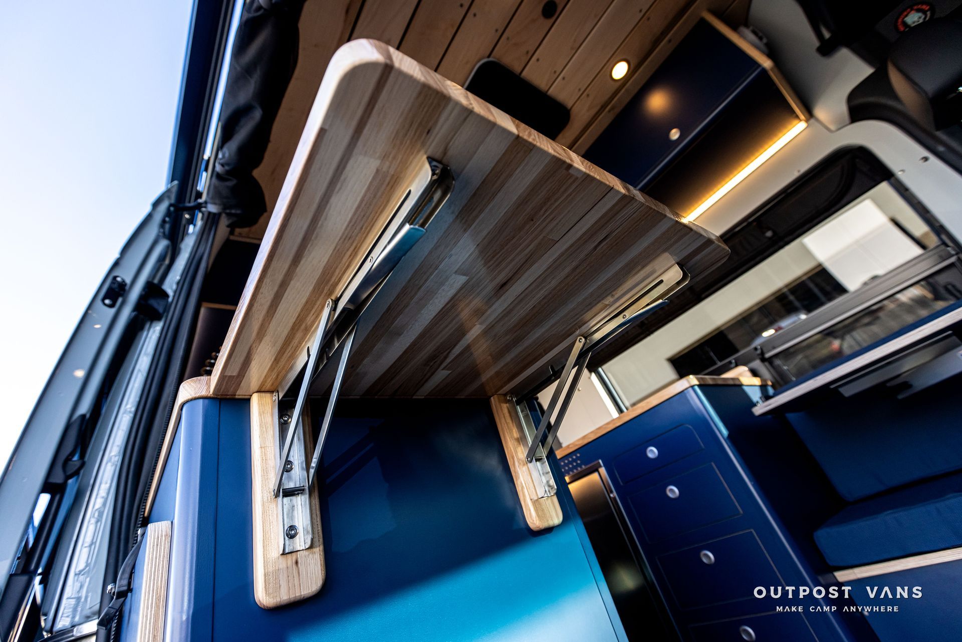 A wooden table is hanging from the side of a van.